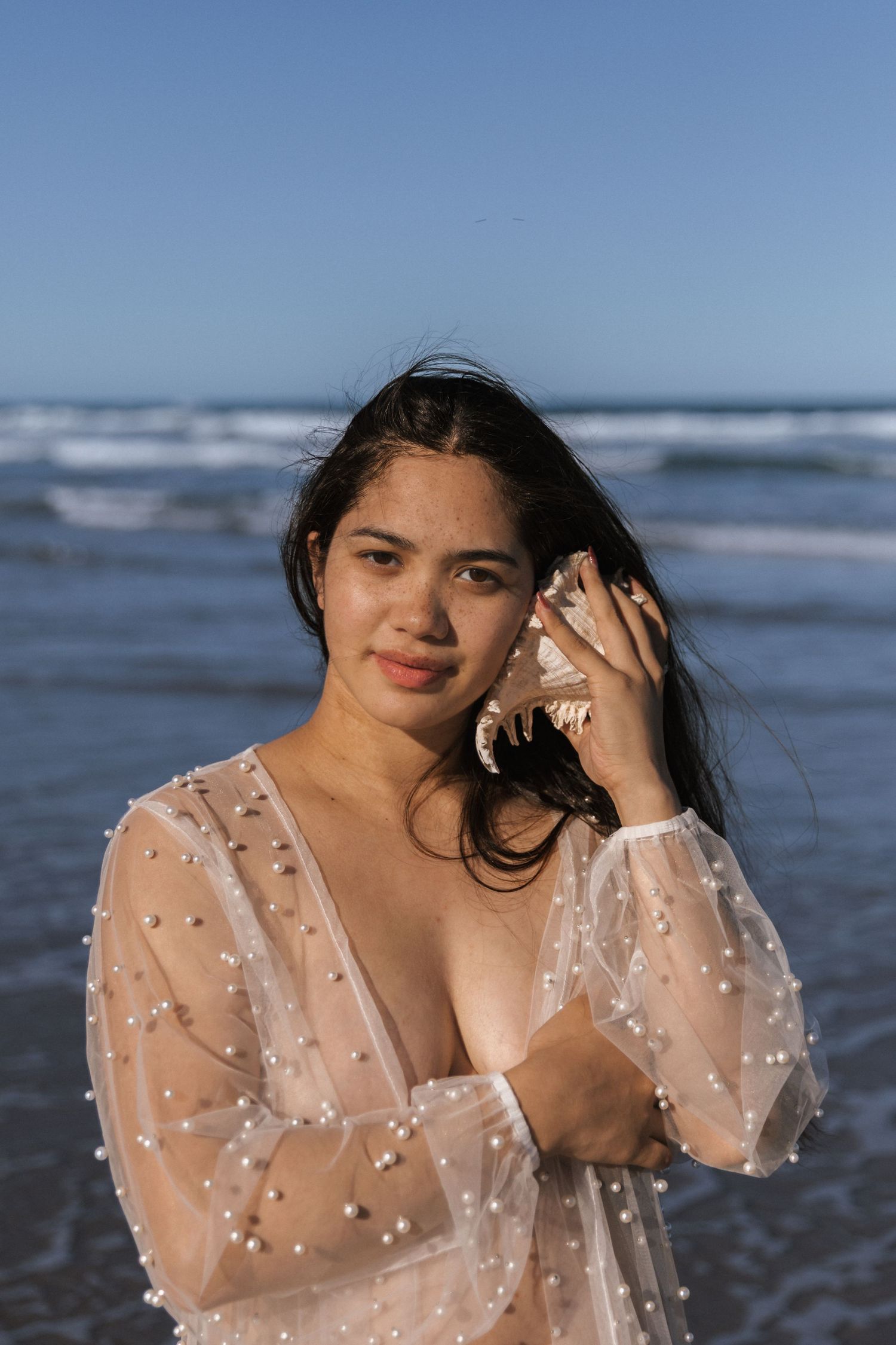 Beach portrait with sheer dotted dress against ocean waves and blue sky.