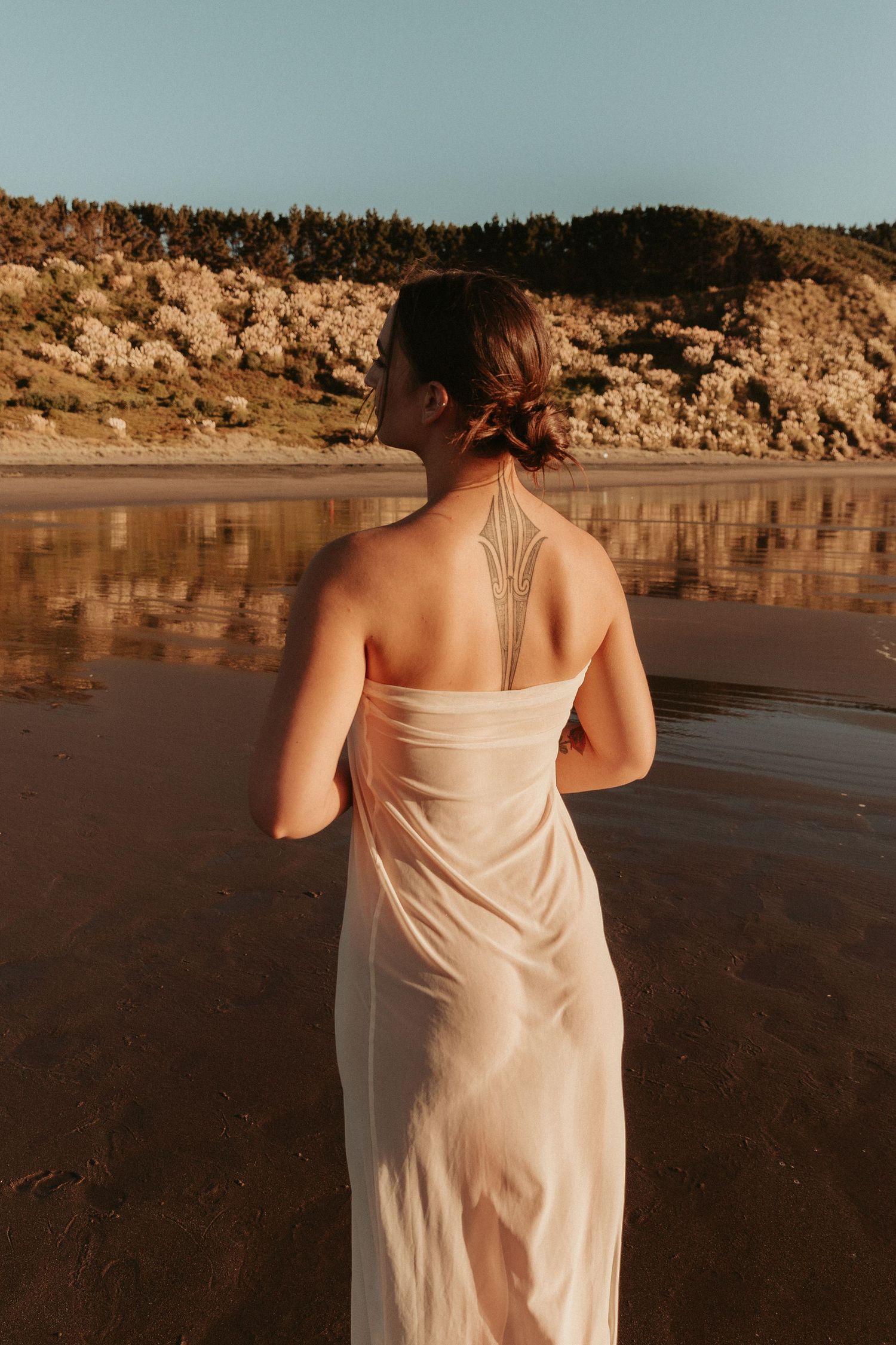 Person in white dress walking along beach shore at sunset with cliffs in background.