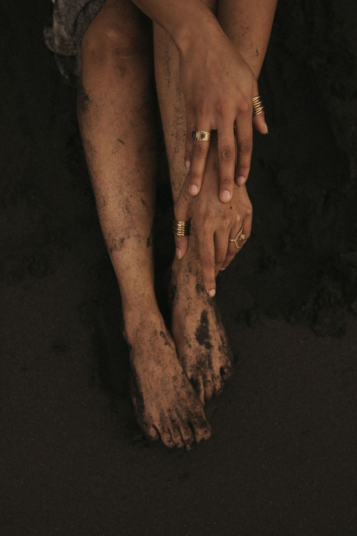 Artistic photo of muddy feet and hands with rings against dark background showing contrast between clean and dirty skin.