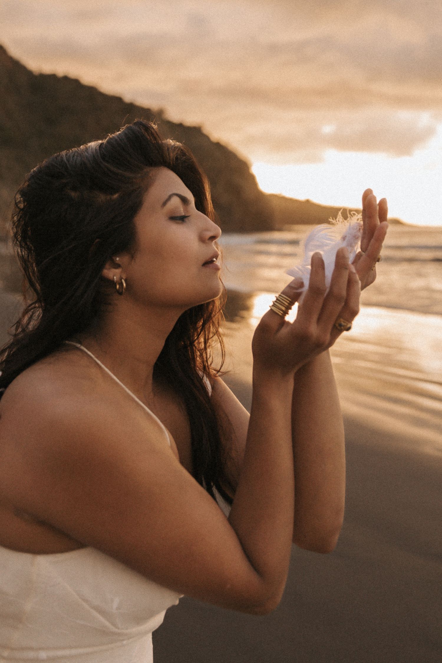 A silhouetted figure in a white dress poses expressively on a beach at sunset with dramatic golden lighting.