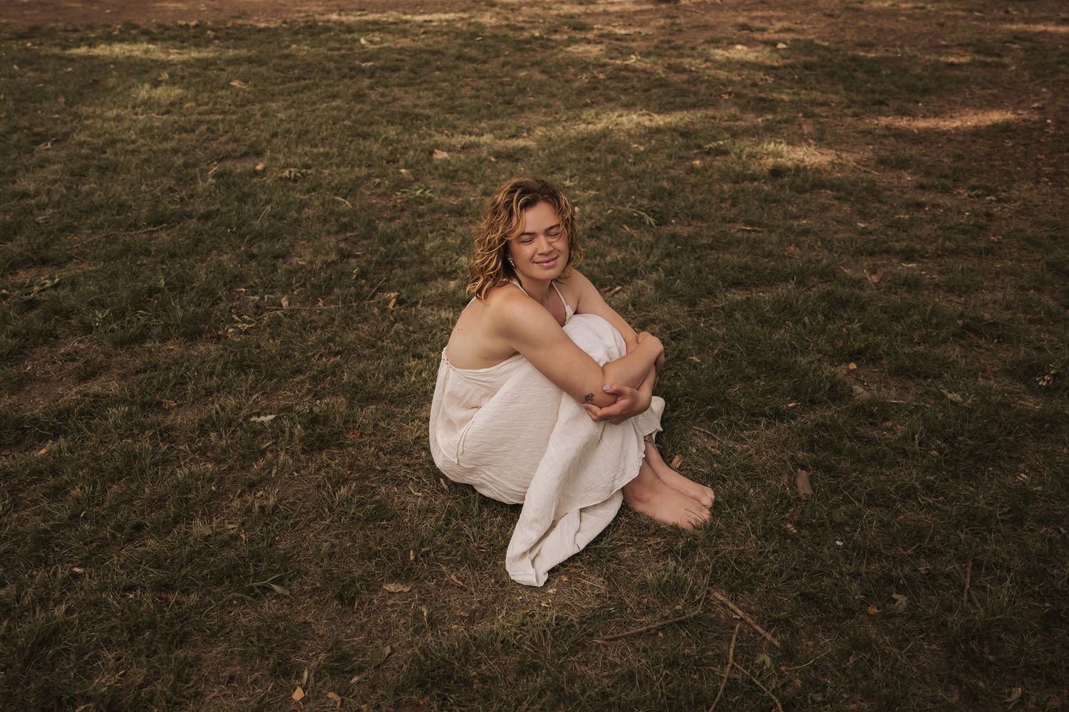 A peaceful portrait sitting on grass in a flowing white dress at sunset.