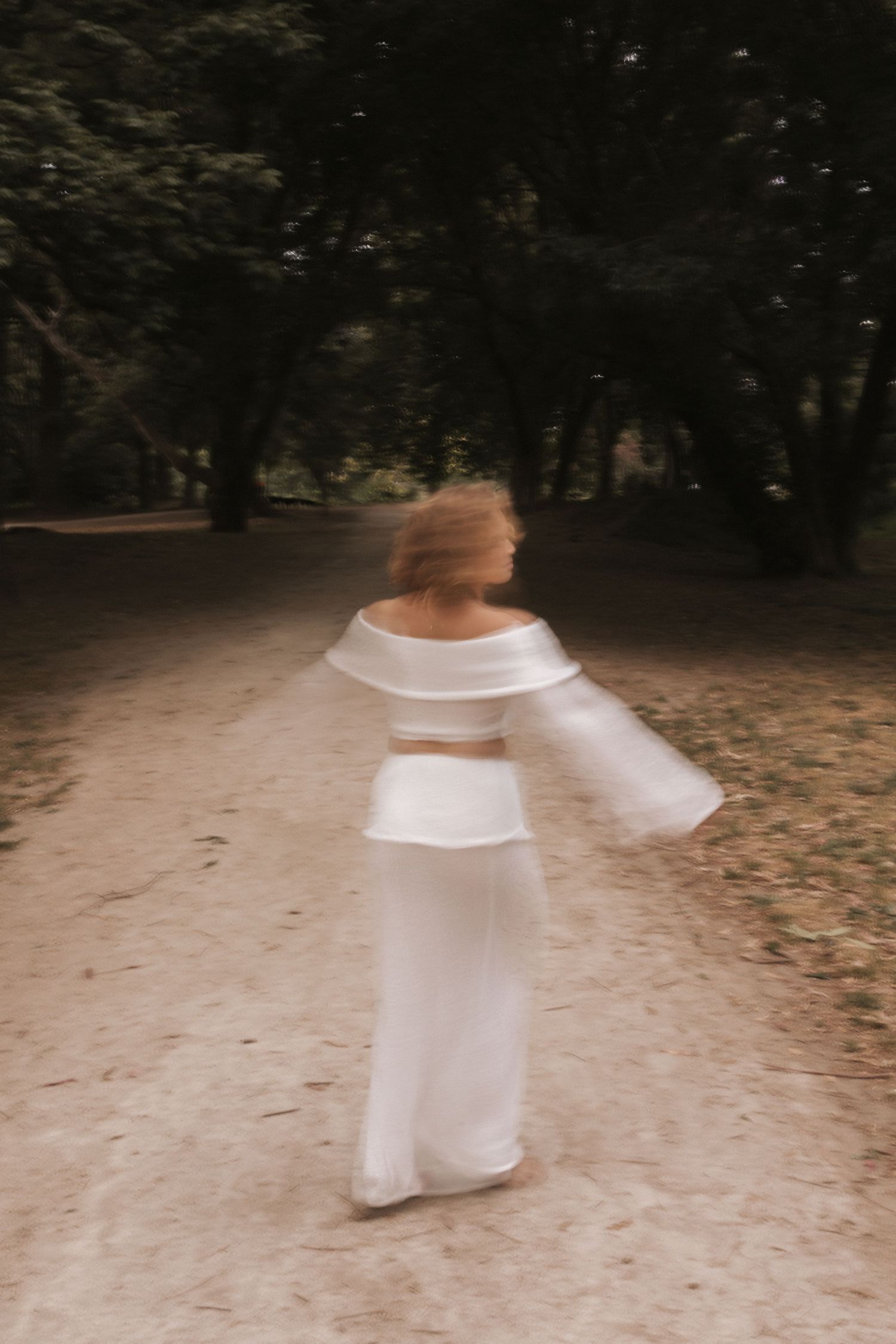 Motion blur photo of person in white outfit twirling on forest path.