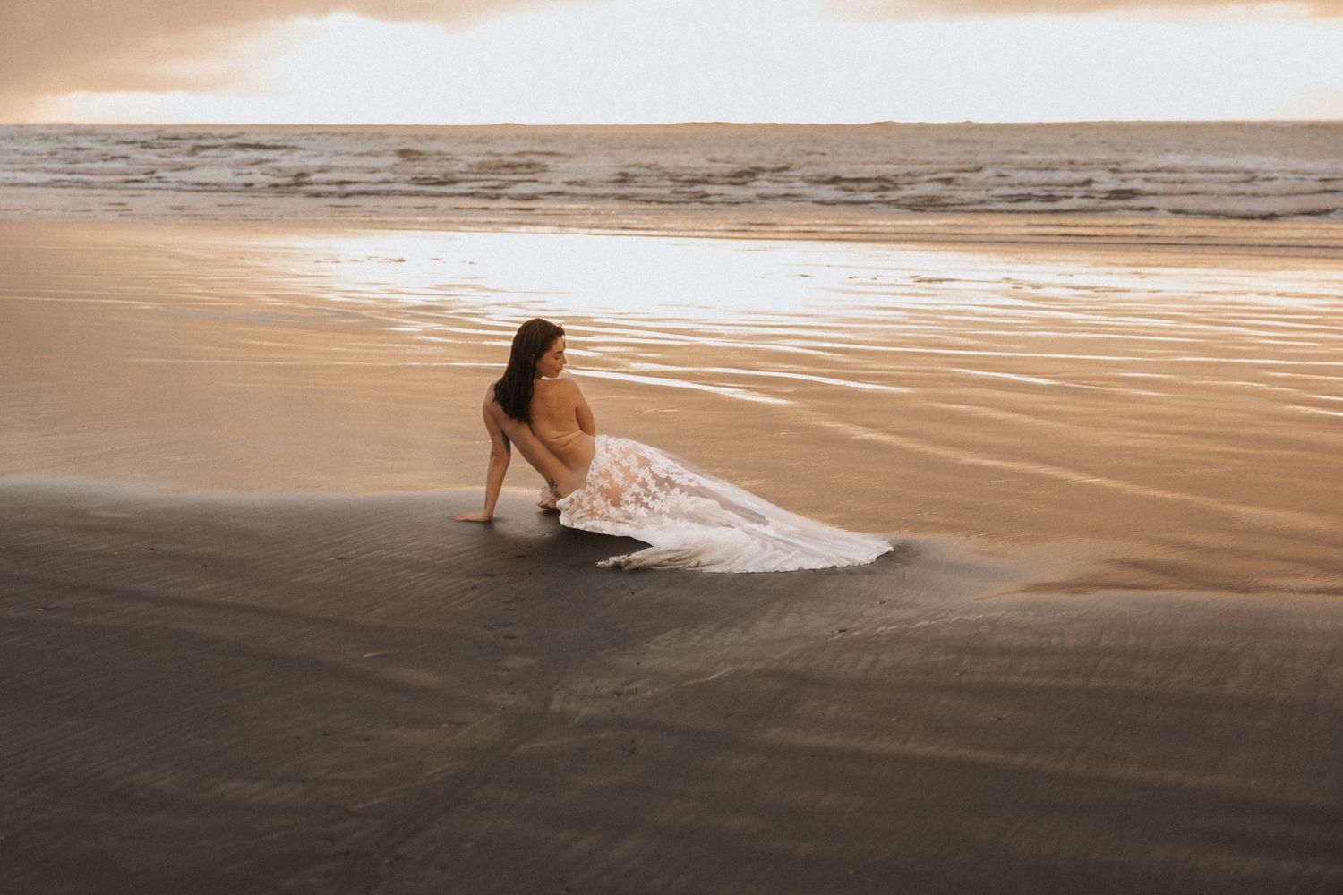 Artistic beach scene with person in flowing dress against golden sunset light.