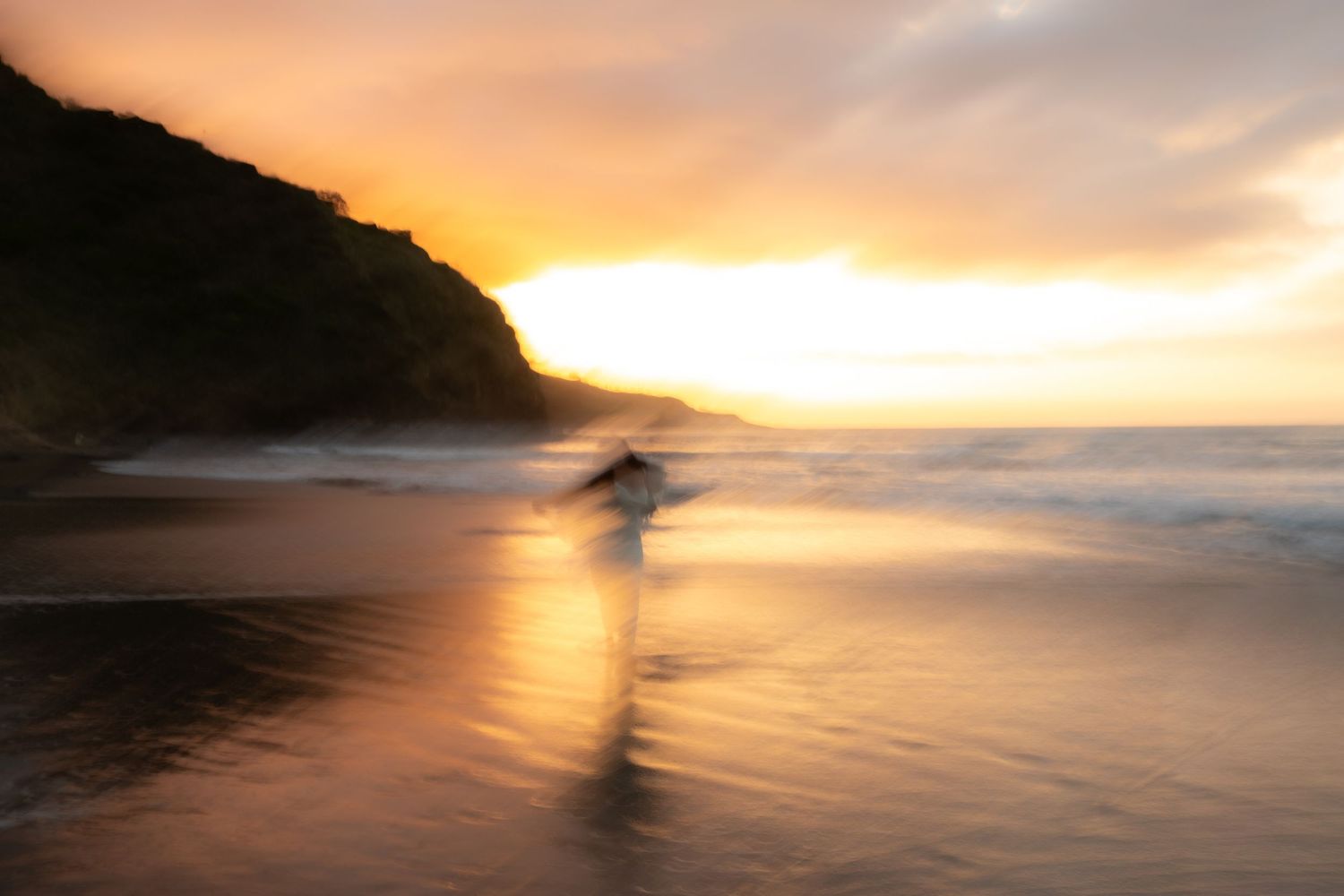 A dramatic orange sunset over the ocean horizon creates silhouettes of coastal cliffs and rocks along the shoreline.