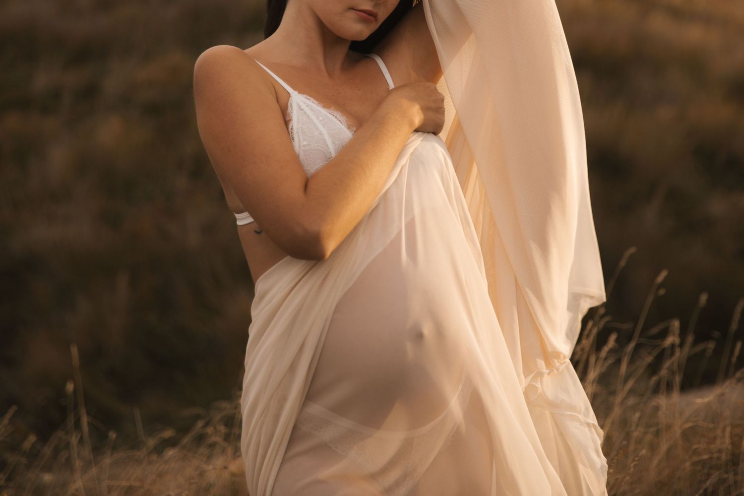 Intimate maternity portrait with delicate white fabric in warm evening light.