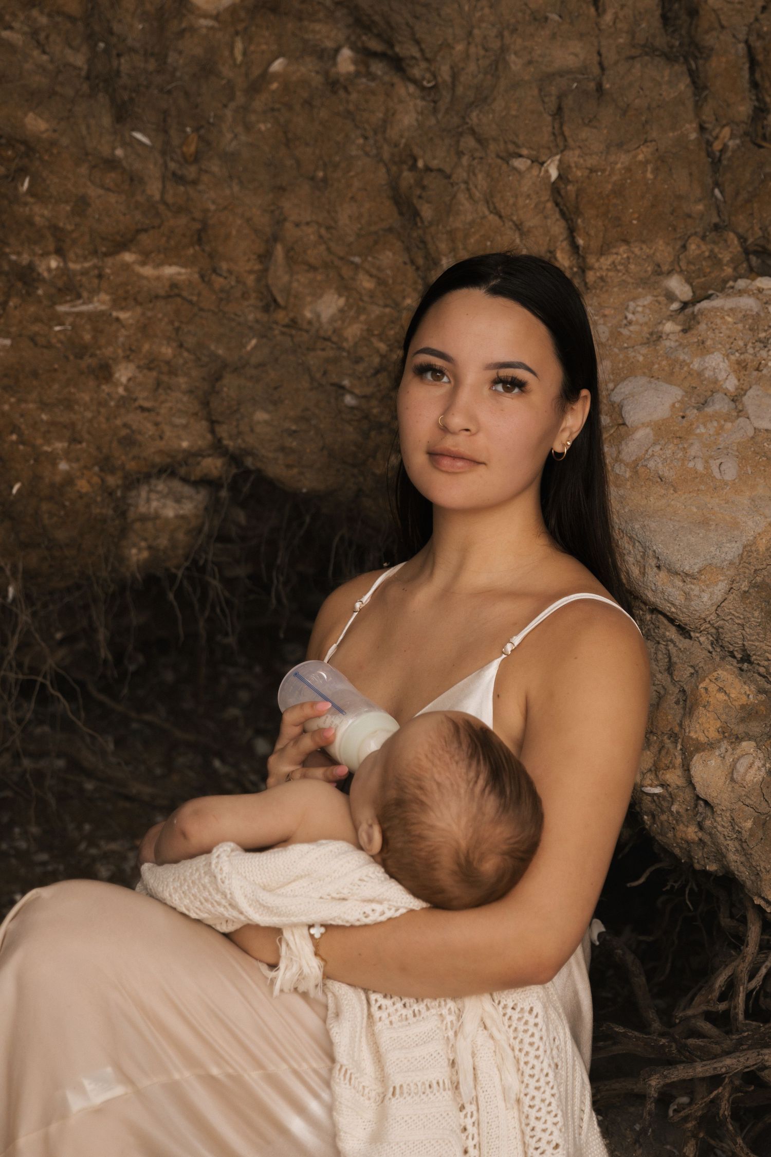 A tender nursing moment captured in a rustic cave setting with soft natural lighting.