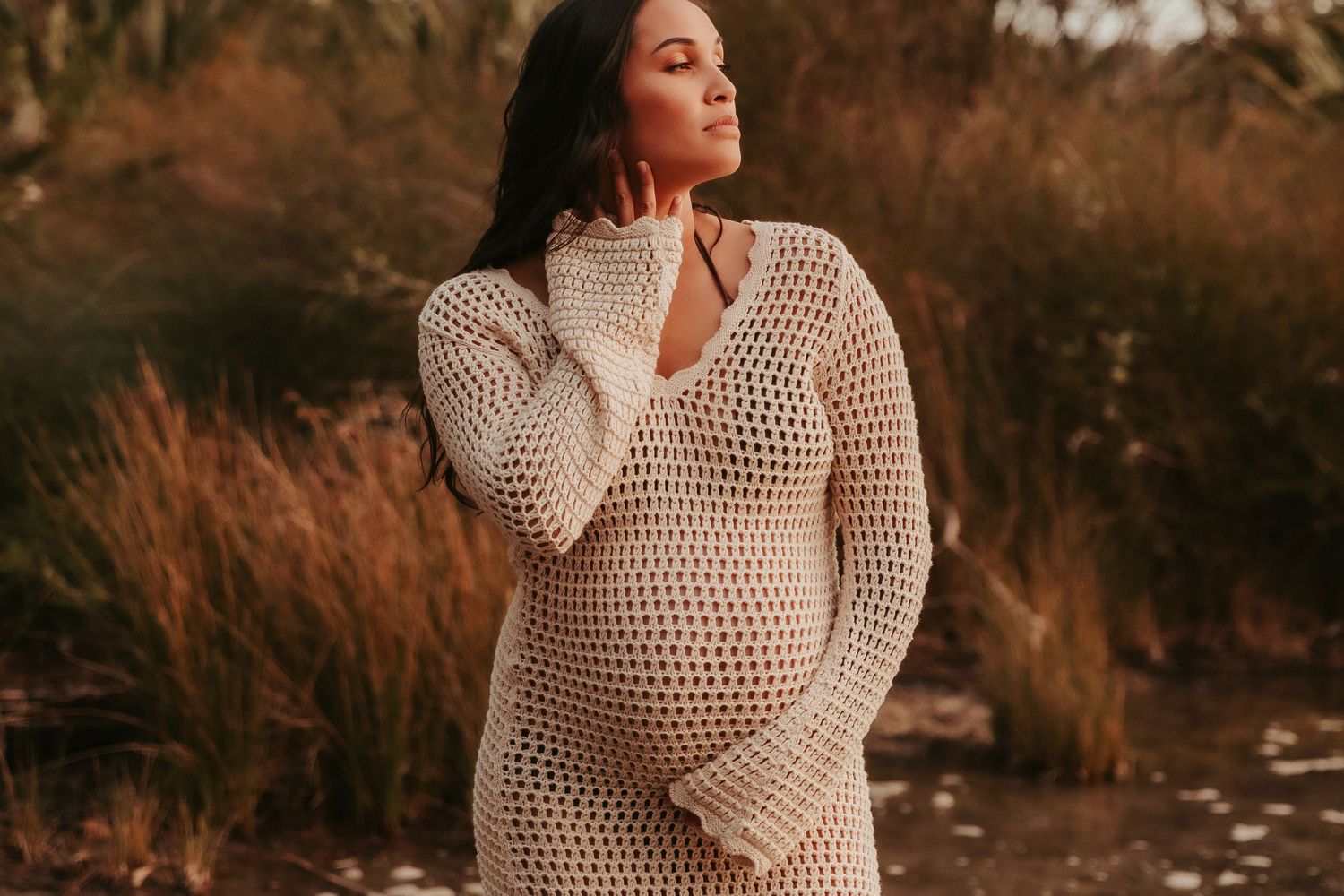 Person in knit sweater poses against autumn backdrop during golden hour photoshoot.