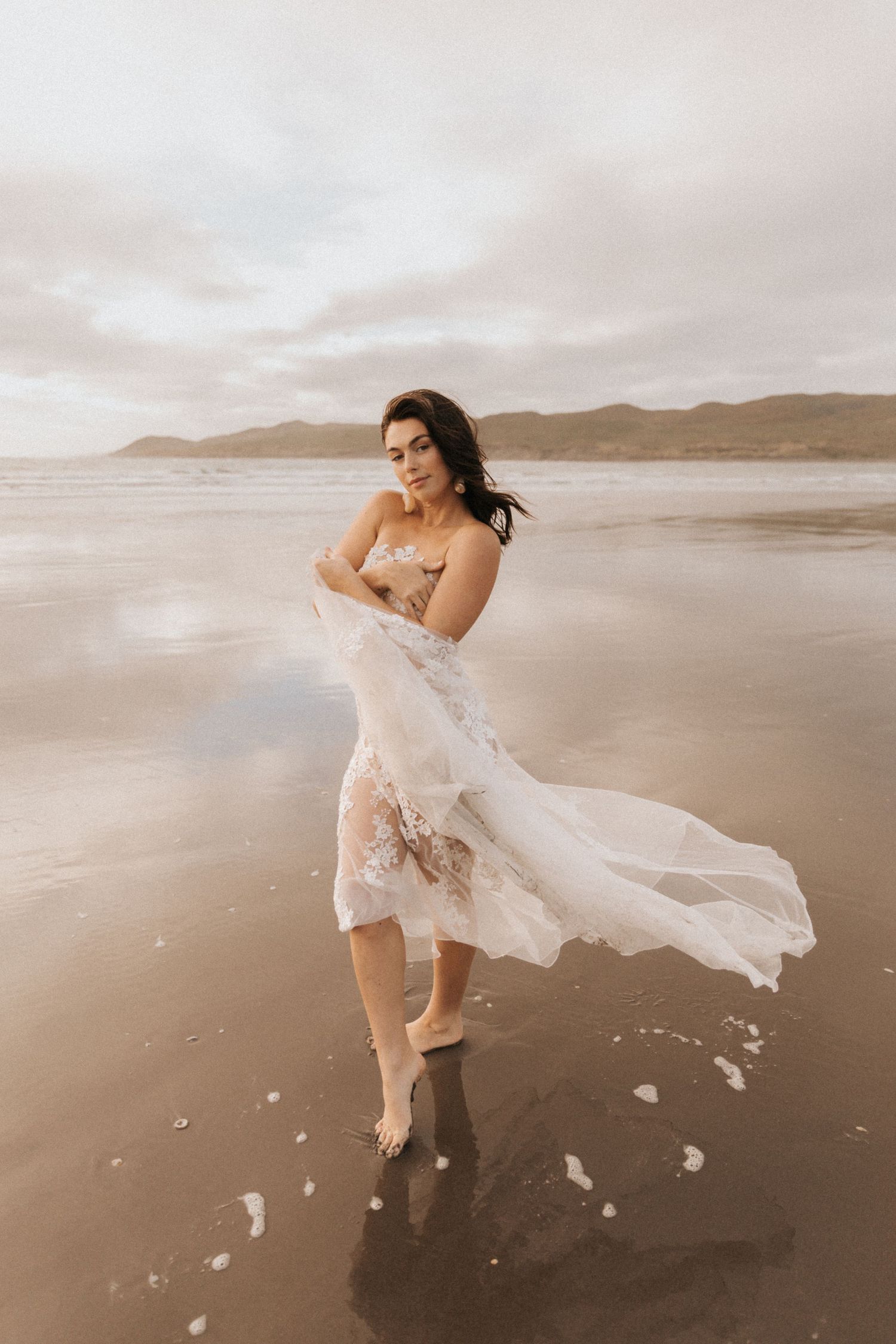 White lace dress billowing in the ocean breeze during a romantic beach photoshoot.