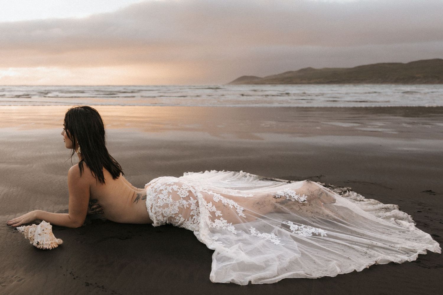 Dramatic beach landscape with white dress against mountainous coastline at sunset.