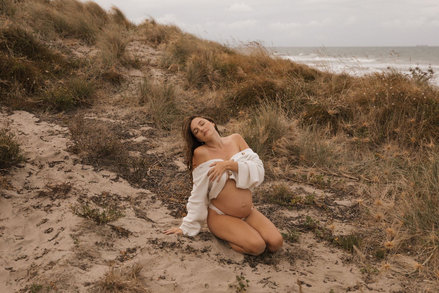 Natural light portrait session on beach with coastal vegetation and cloudy sky.