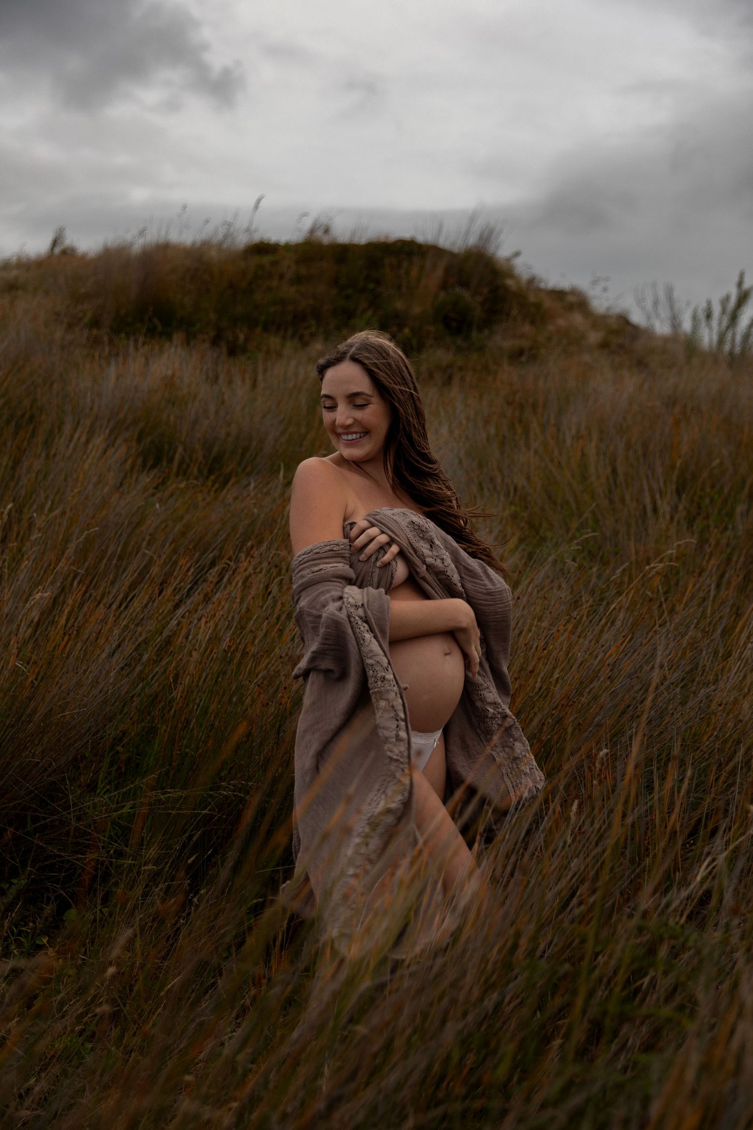 Moody photoshoot in tall grass field with cloudy sky backdrop.