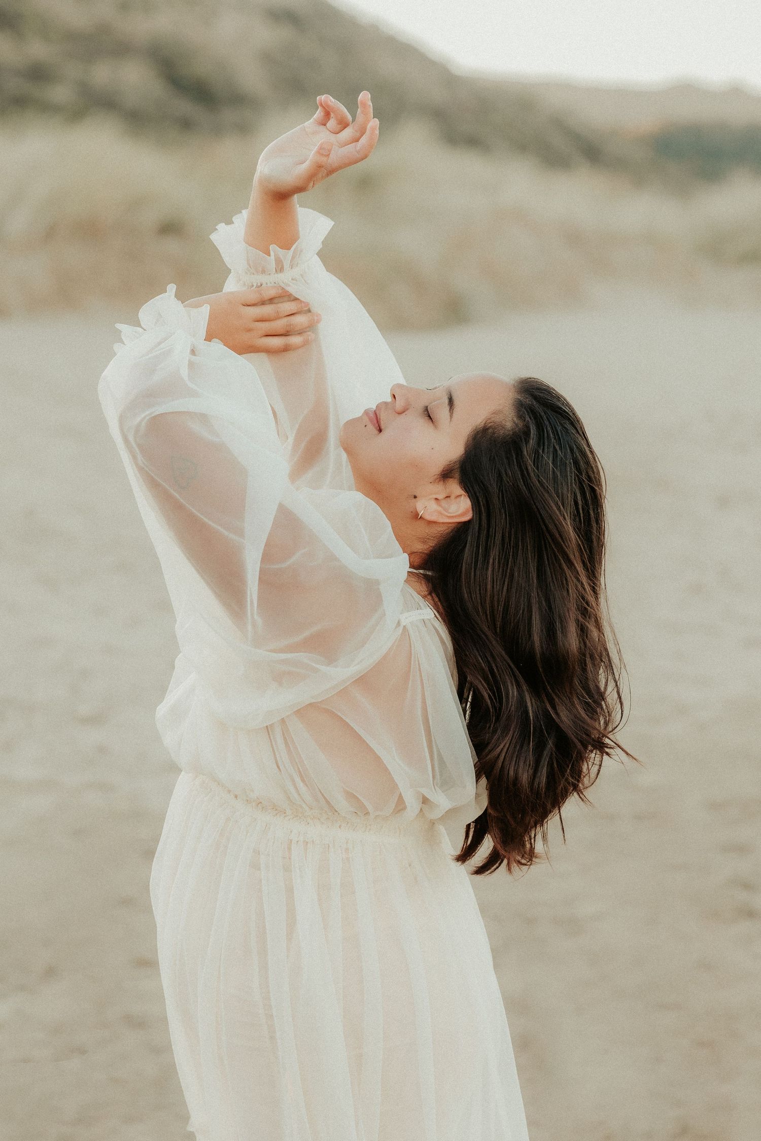 Expressive dance-like movements captured in flowing white dress on sandy terrain.