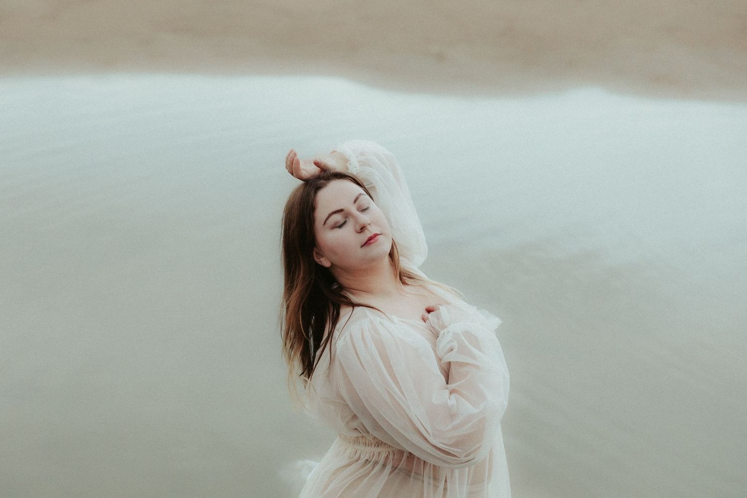 Ethereal movement captured in cream-colored dress against misty beach backdrop.