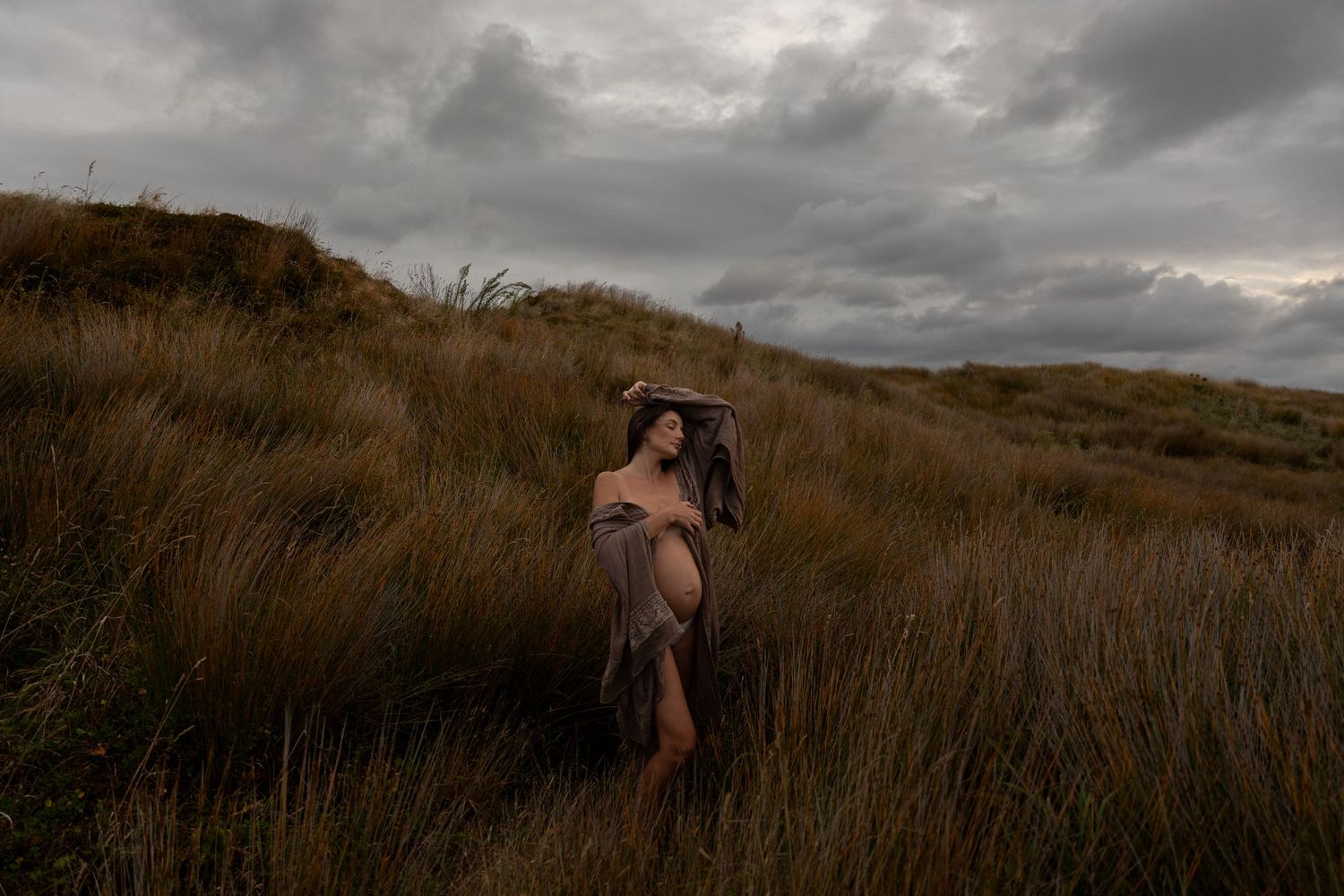 Moody landscape photography with tall grass against stormy skies at dusk.