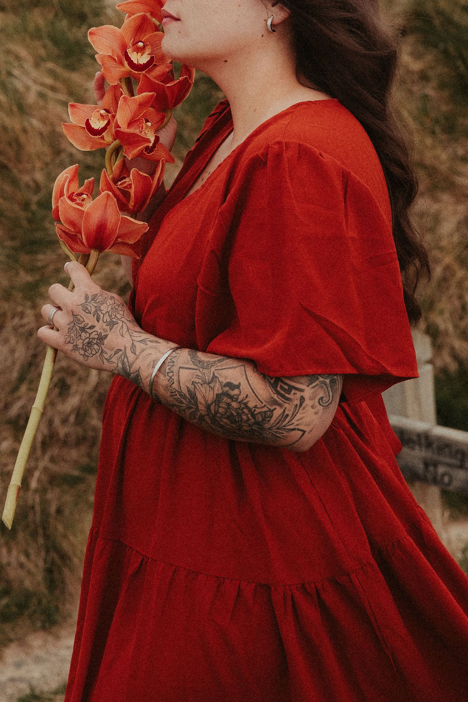Person in flowing red dress holding orange orchids showing tattooed arm.