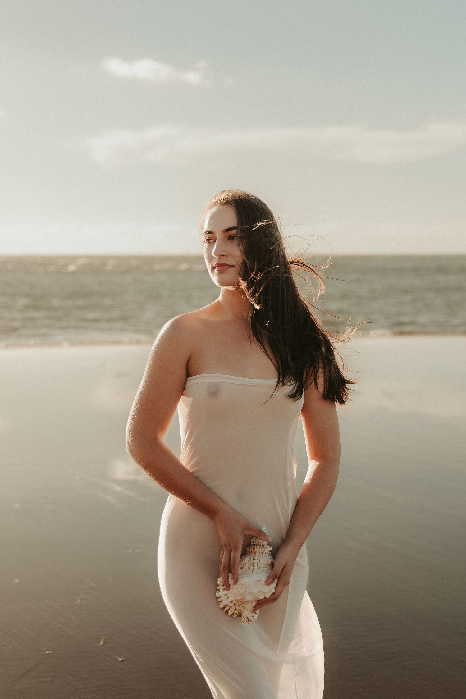 Windswept maternity portrait on beach with golden sunset lighting.