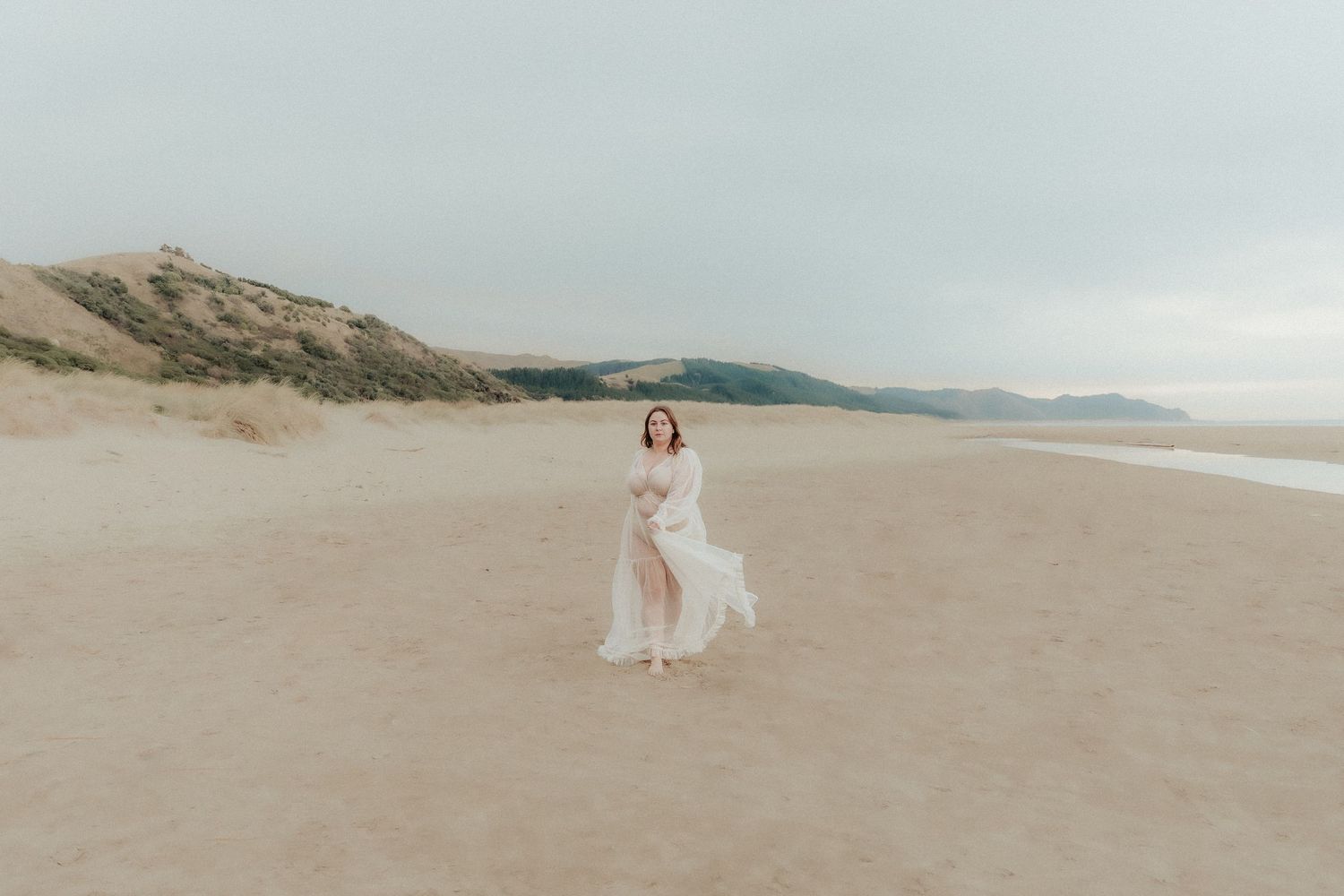 Wide landscape shot of beach photoshoot with white dress against coastal cliffs.
