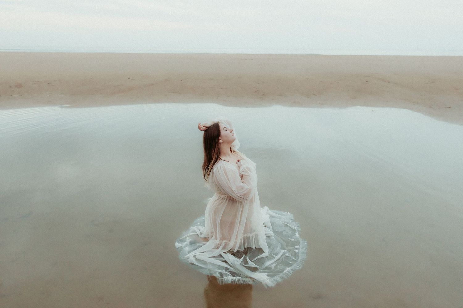 Artistic water portrait session featuring flowing fabric and gentle ocean waves.