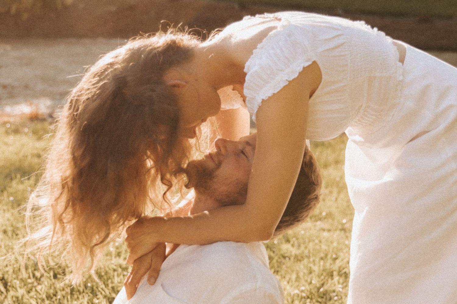 A couple in white outfits dance and embrace in a sunlit meadow during golden hour.