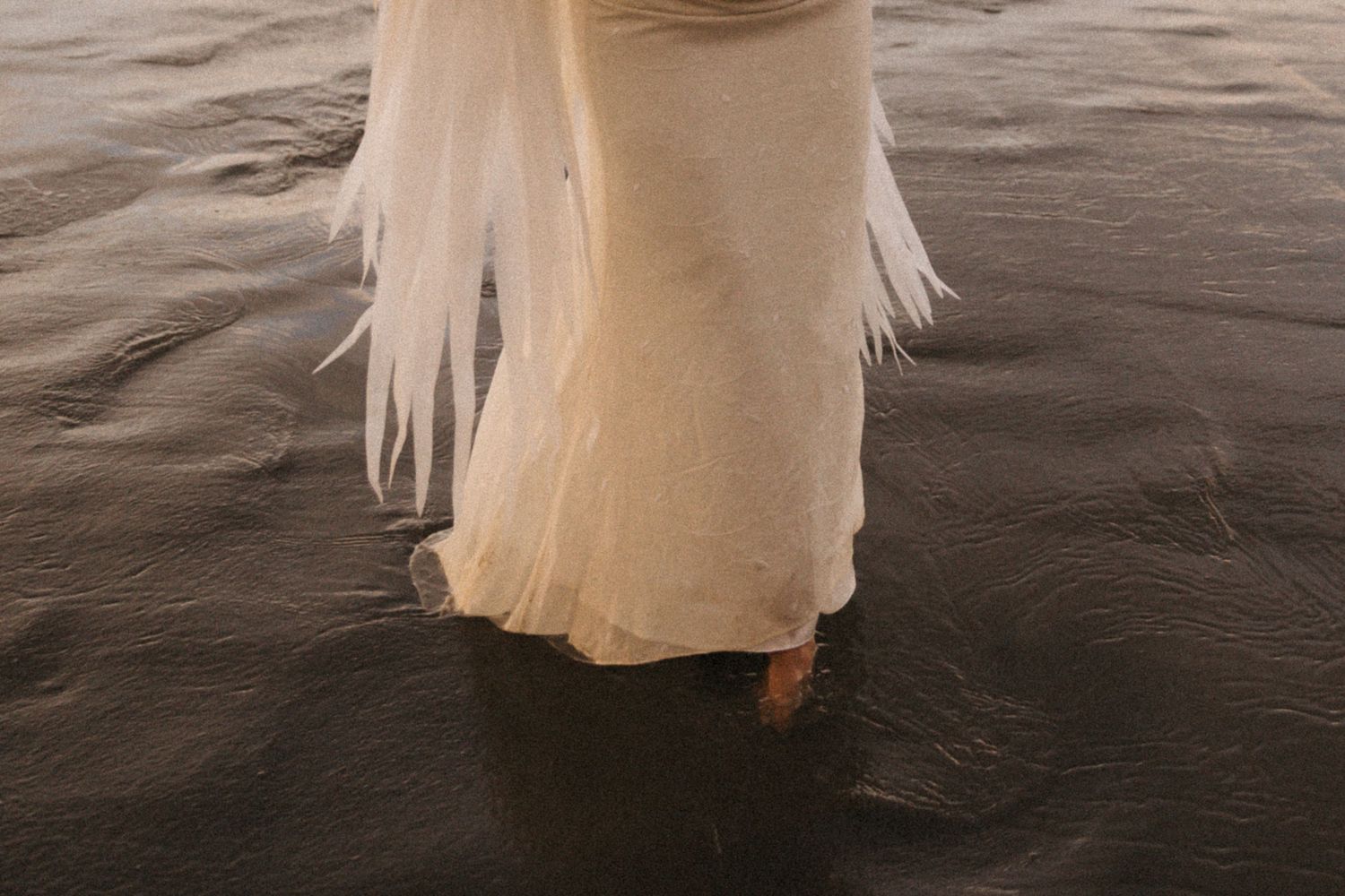 A person in a flowing white dress stands at the edge of dark water creating a dreamy ethereal scene.
