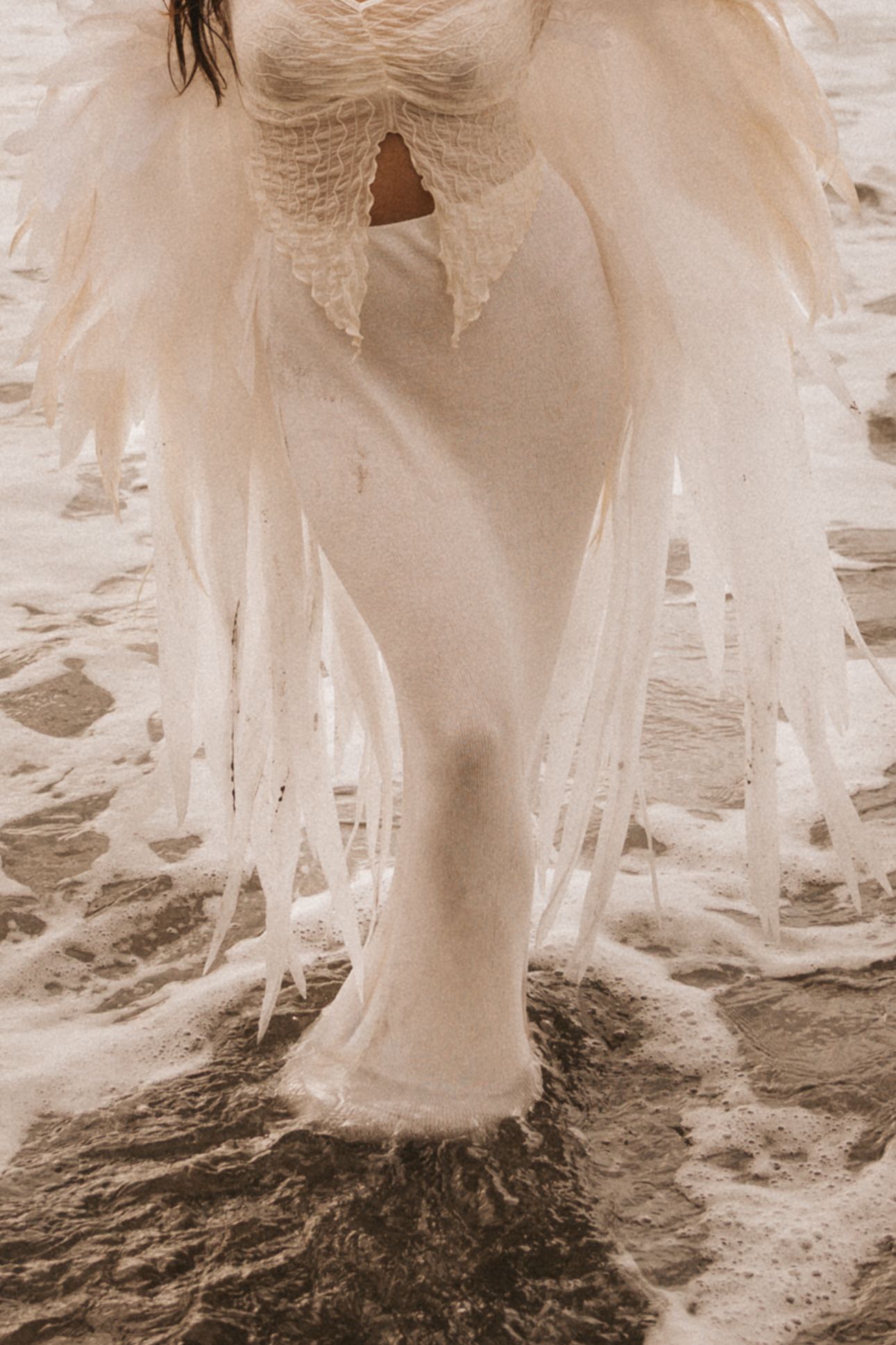 A sepia-toned close-up of flowing white wedding dress fabric and lace details trailing on the ground.