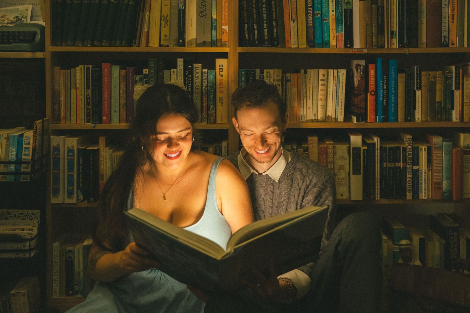 People read together in a cozy library surrounded by wooden bookshelves and warm lighting.