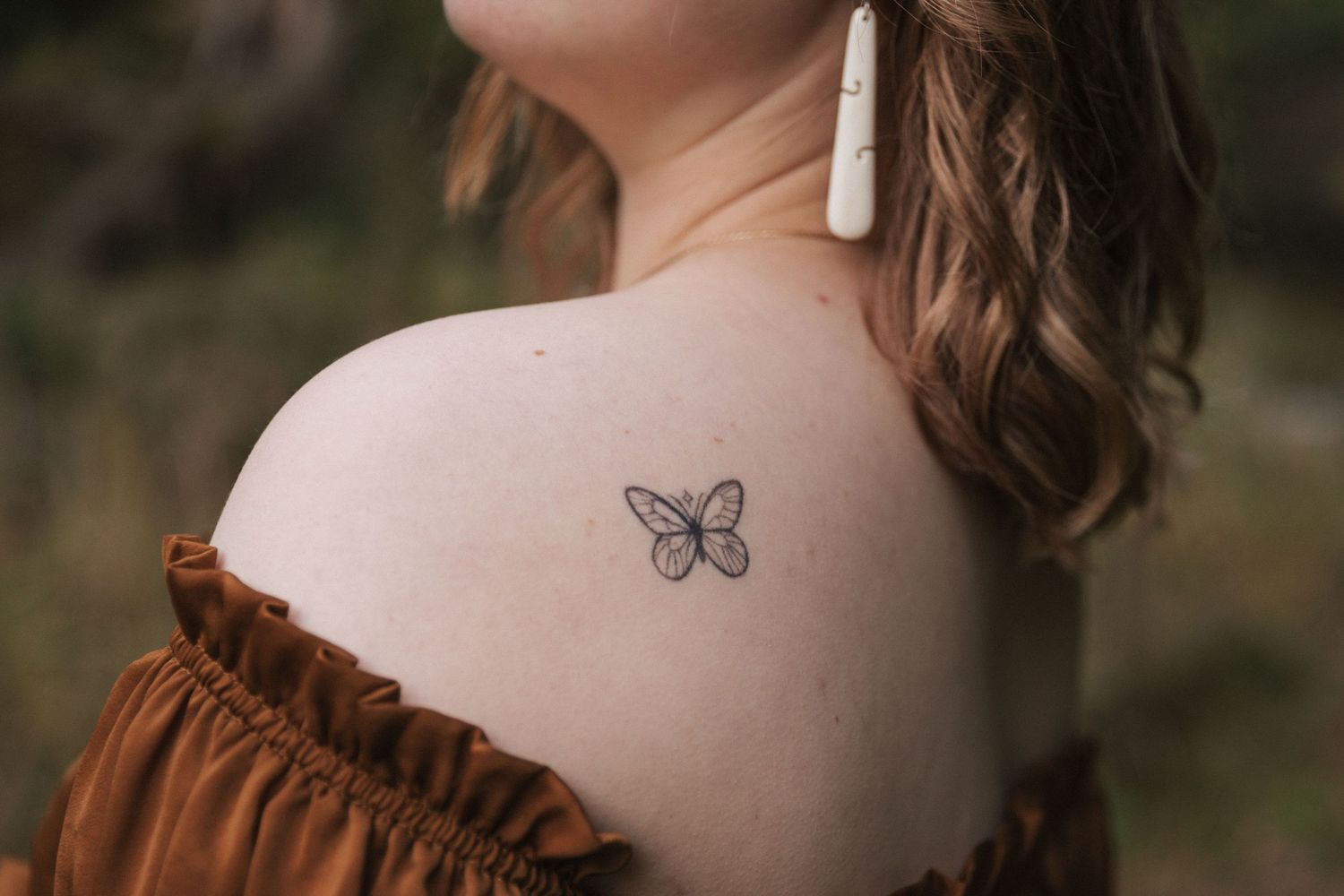 Close-up detail shot showing a butterfly tattoo and brown dress strap against pale skin.