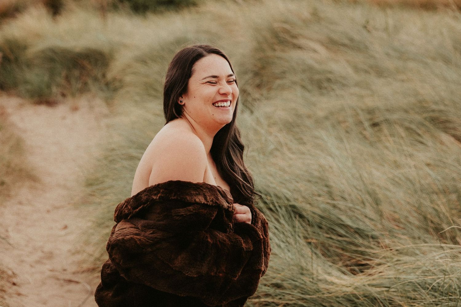Ethereal photoshoot on a beach with flowing brown dress against natural dunes and grasses.