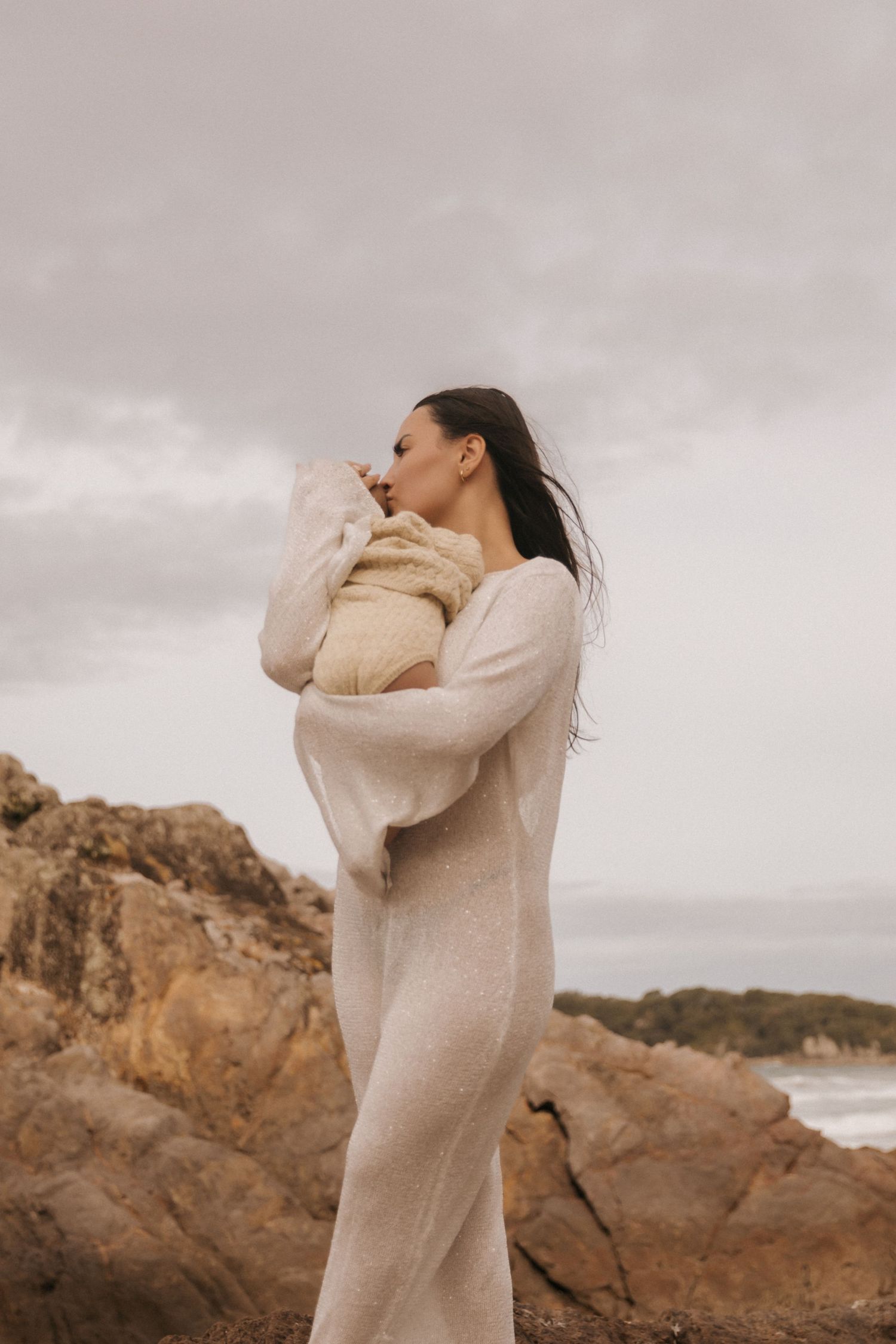 Dreamy overcast beach photoshoot with cream-colored knitwear and rocky backdrop.