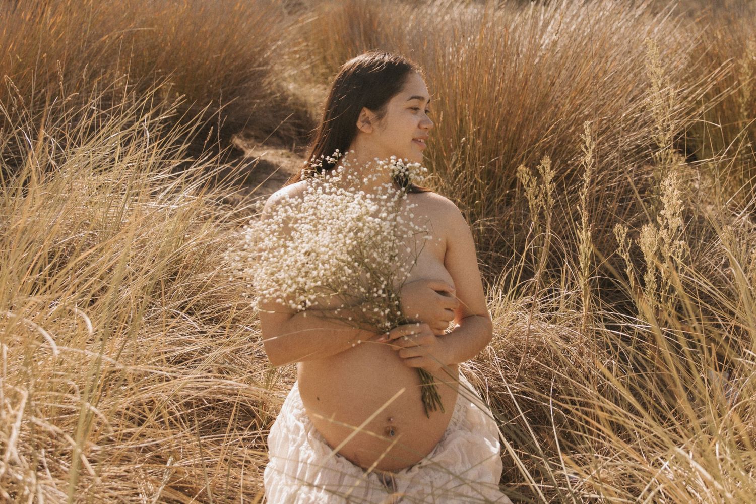 Outdoor maternity portrait with baby's breath flowers in golden autumn field.
