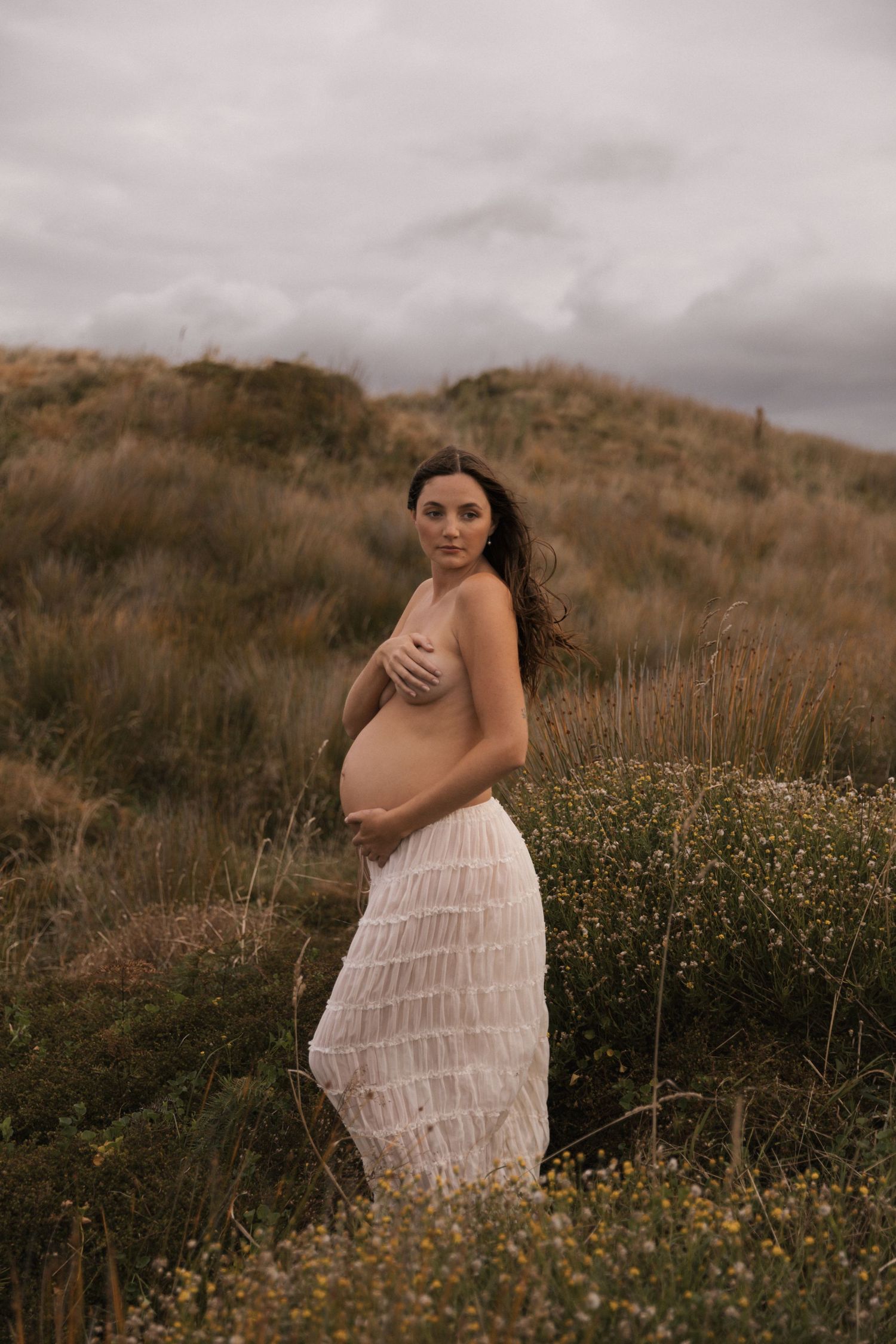 Dreamy outdoor maternity session among yellow wildflowers on a hillside.