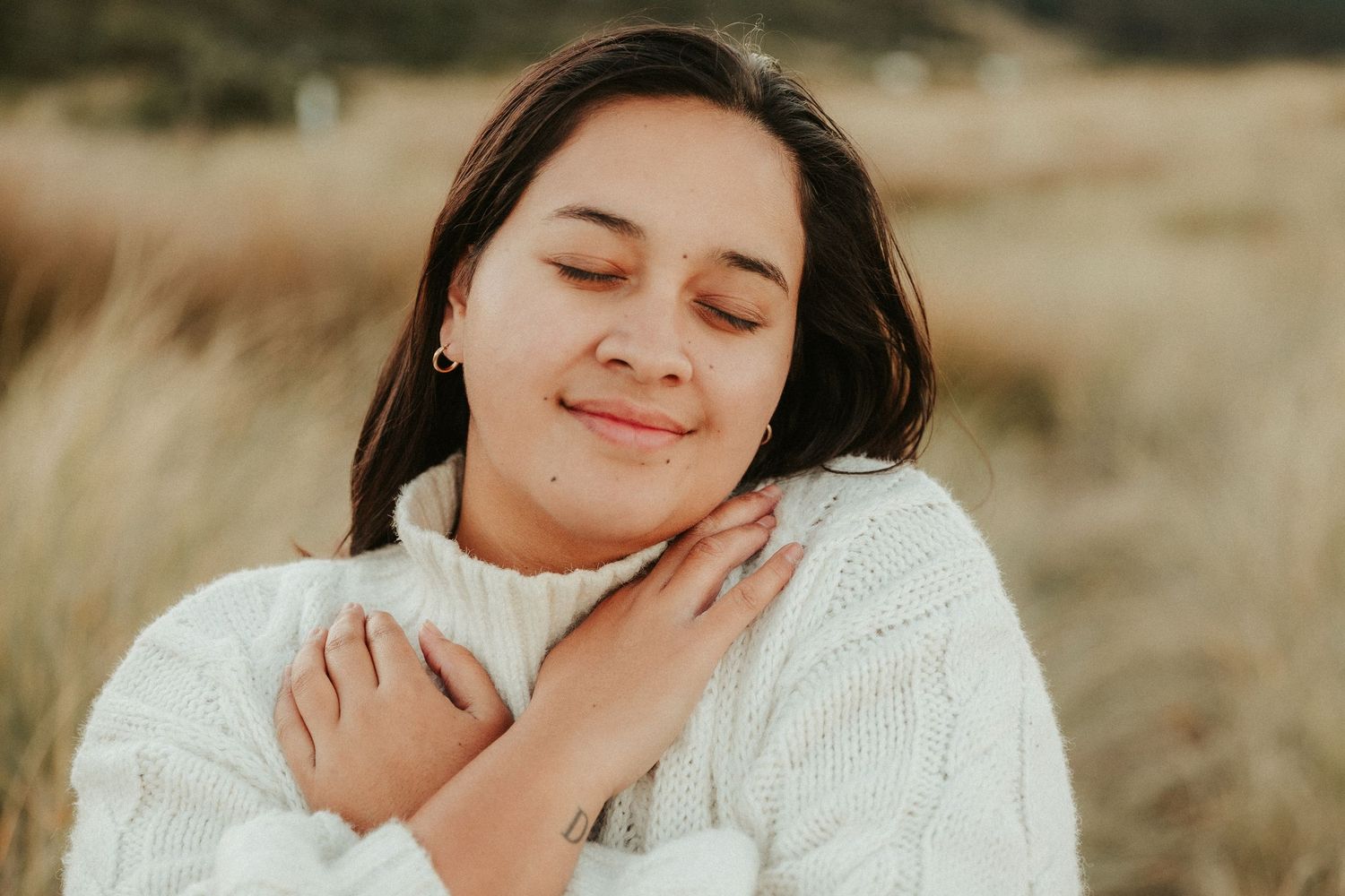 Person in white sweater poses serenely against golden field.