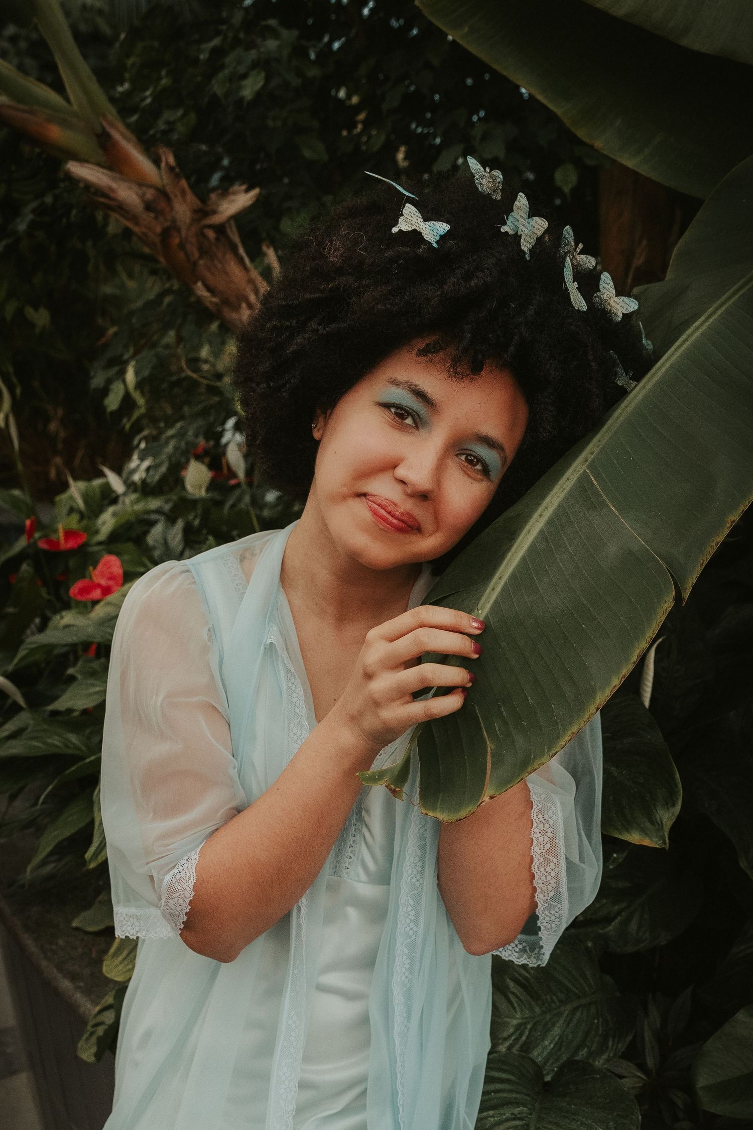 A dreamy portrait among lush green leaves and red flowers in a garden setting.