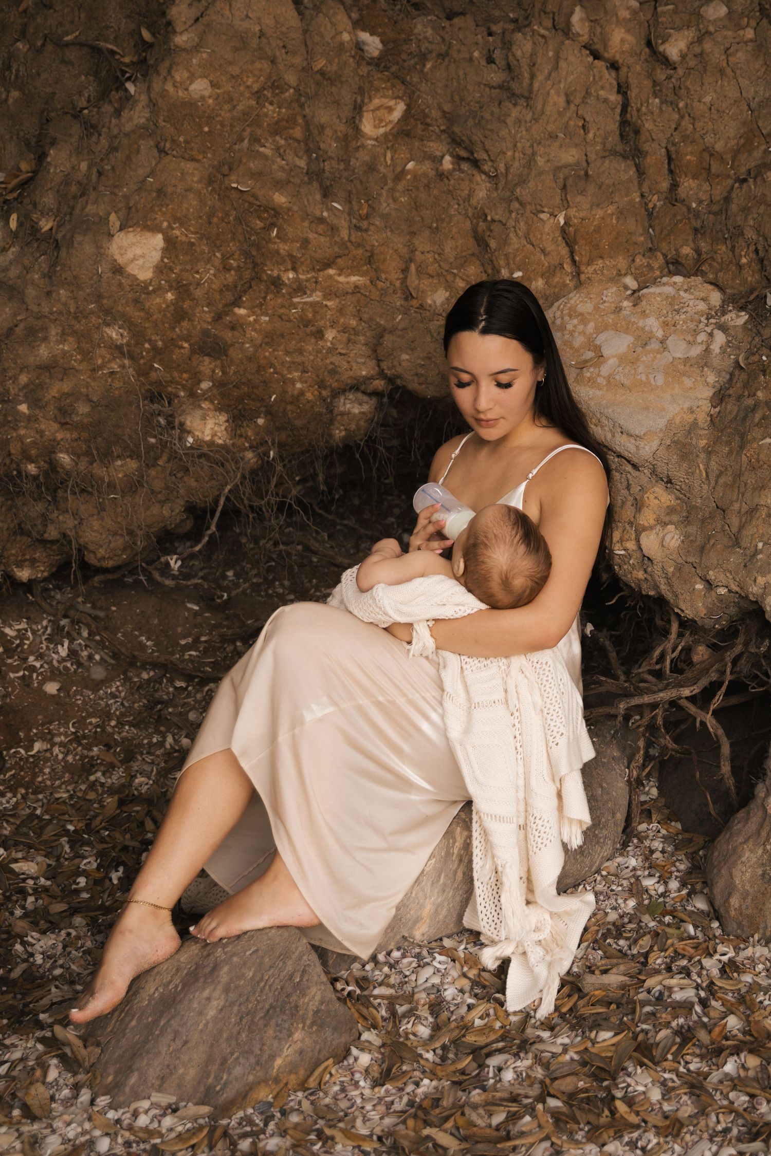 Dreamy portrait session on rocky beach with white flowing dress and natural textures.