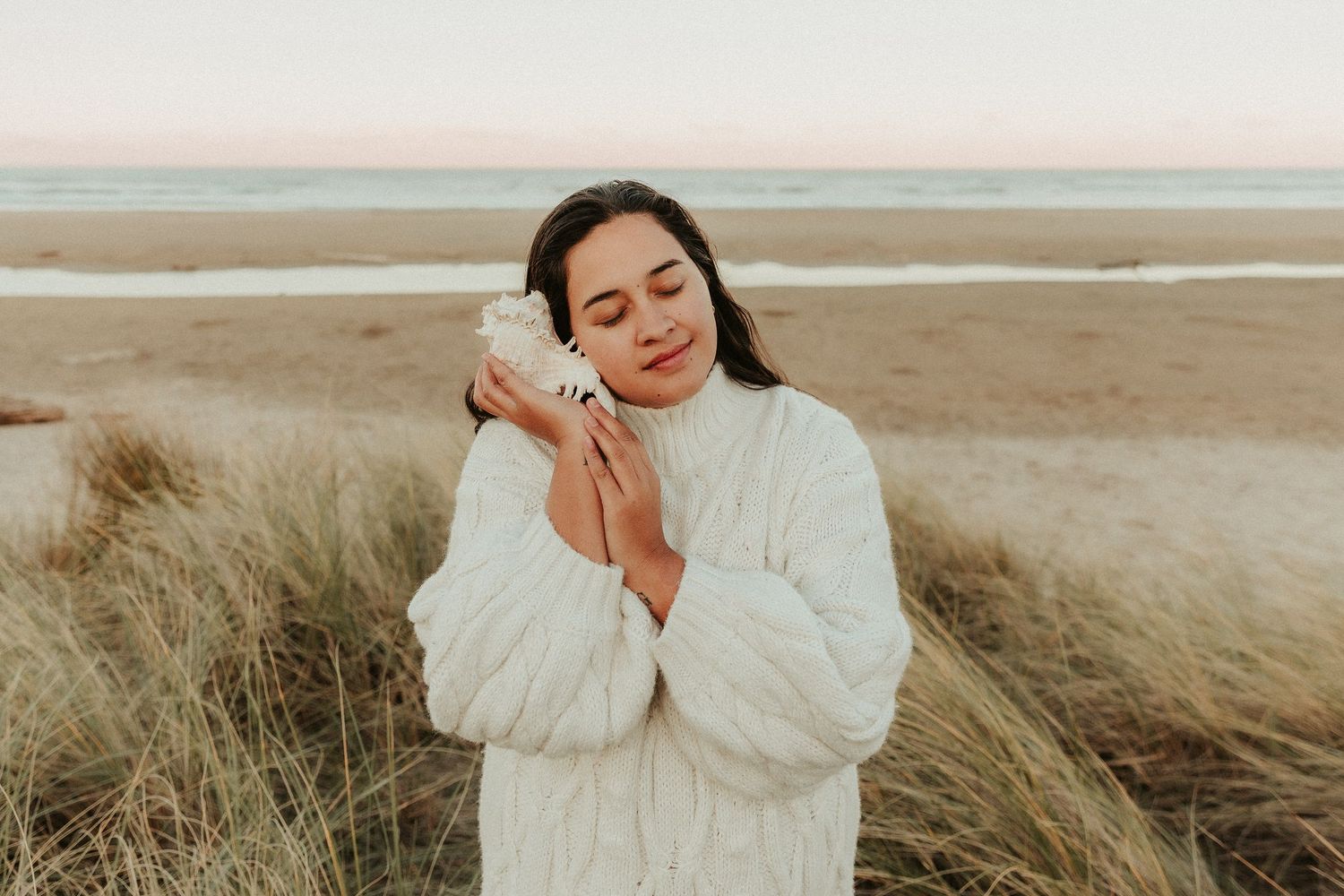 Dreamy beachside portrait with soft white sweater against coastal landscape.