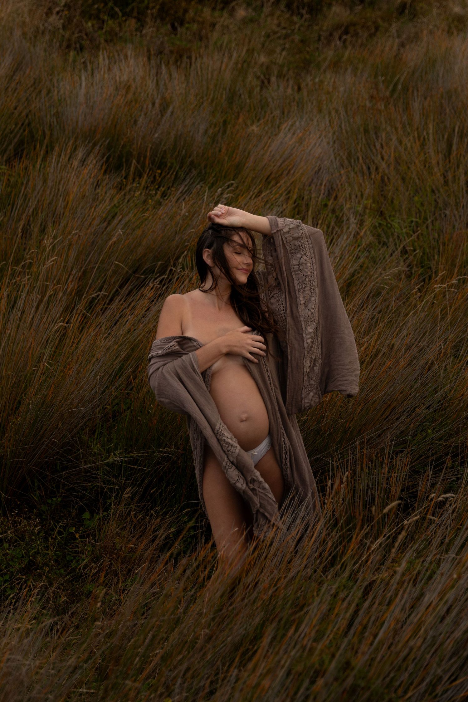 Artistic portrait in tall grass field with moody brown tones and natural lighting.
