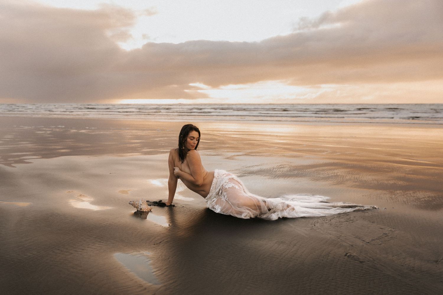 Ethereal beach photography with white dress flowing on dark sand at sunset.