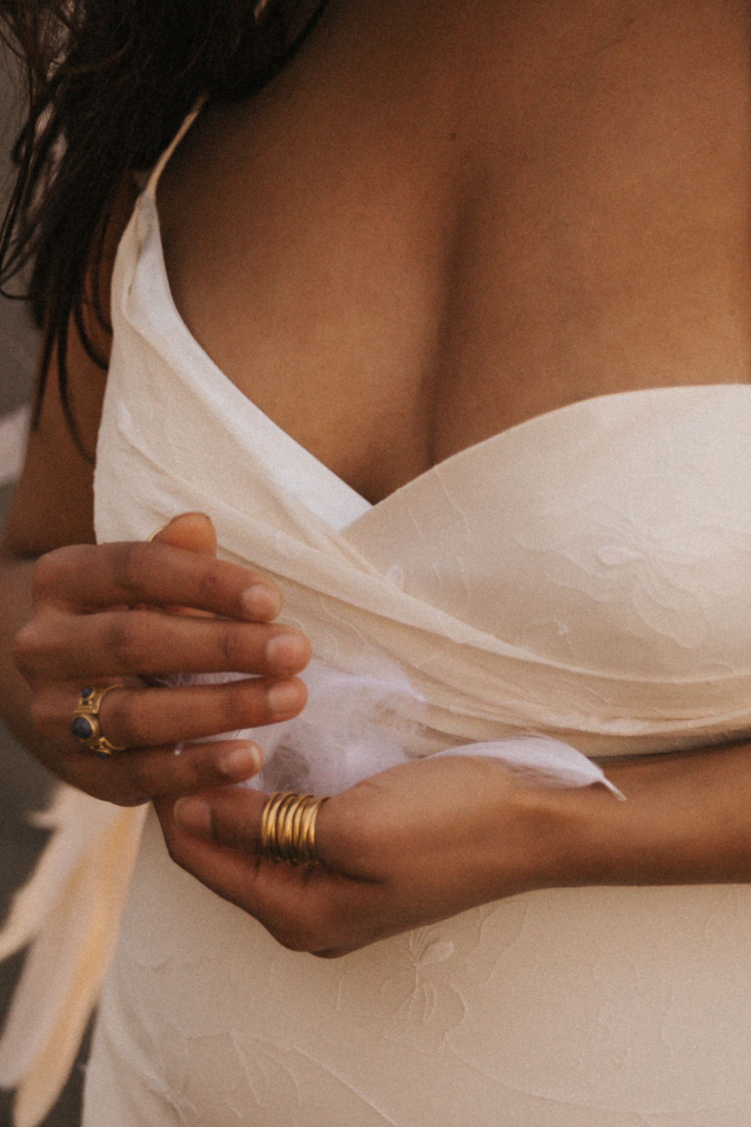 Close-up of hands wearing gold rings and stacked bands against a white dress bodice.