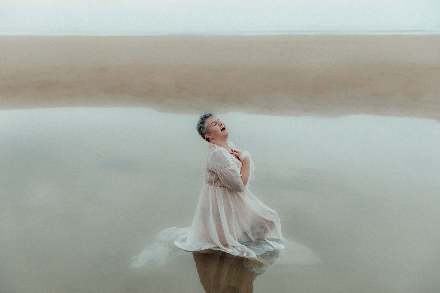 Person in flowy dress poses dramatically while standing in misty water.