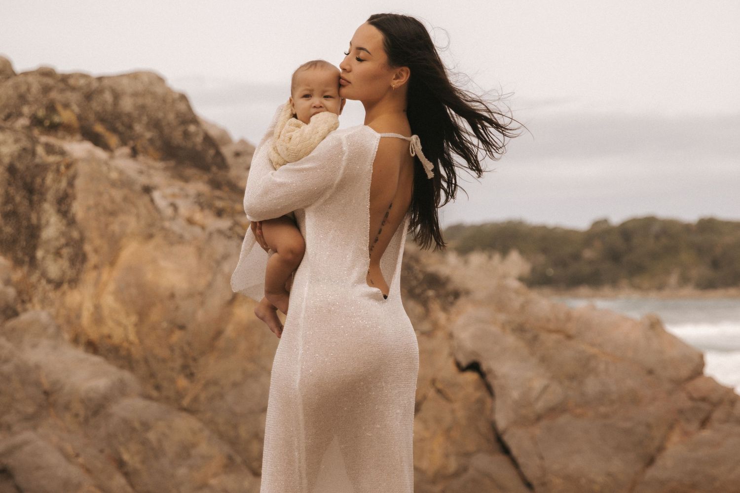 Coastal photography session featuring flowing cream dress against dramatic rock formations.