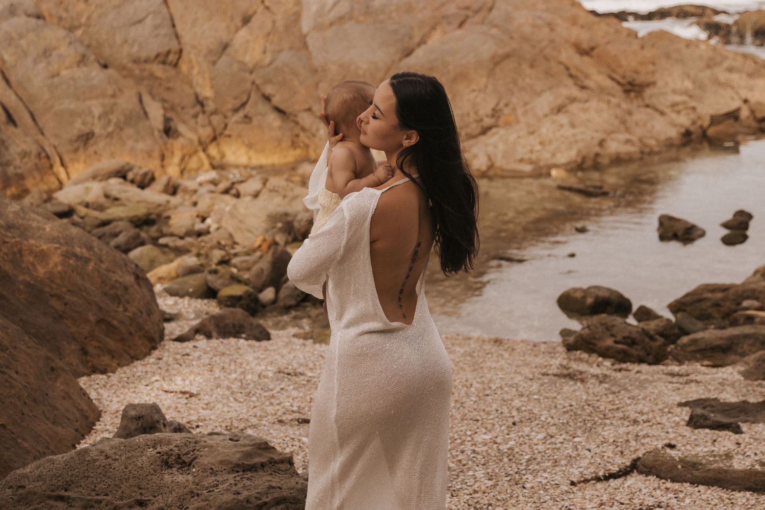 Serene coastal photoshoot with white dress against rocky beach landscape.