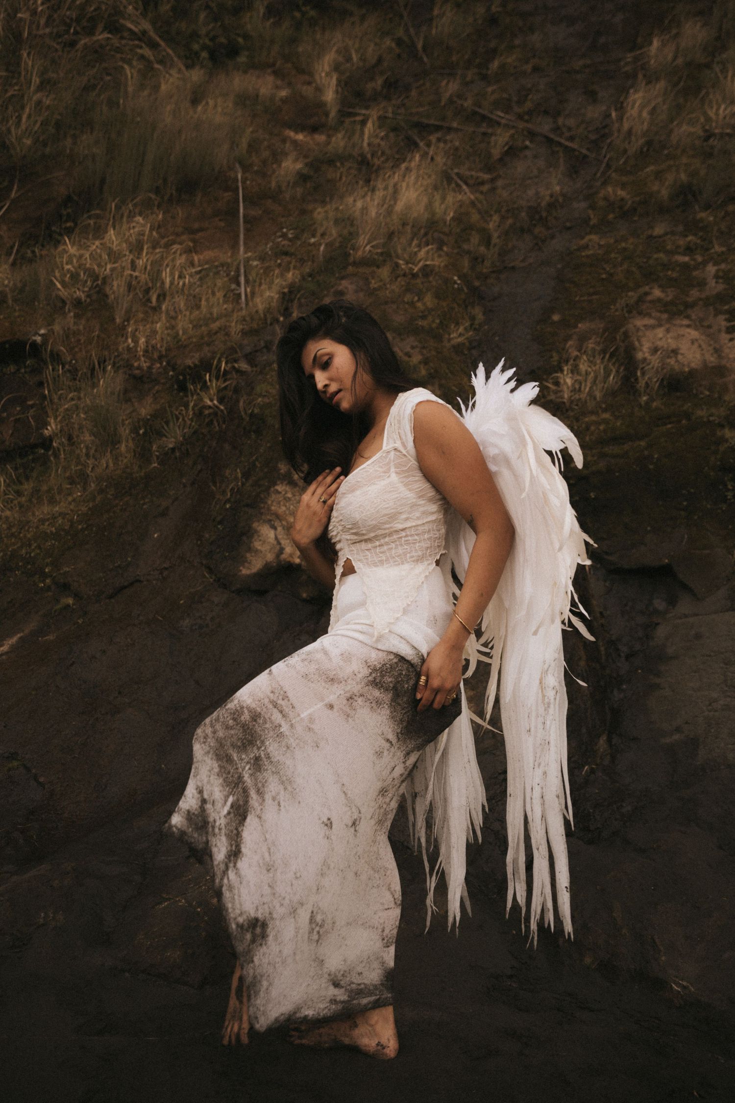 A figure in a white dress and angel wings poses dramatically against a dark cave wall in an artistic photo series.