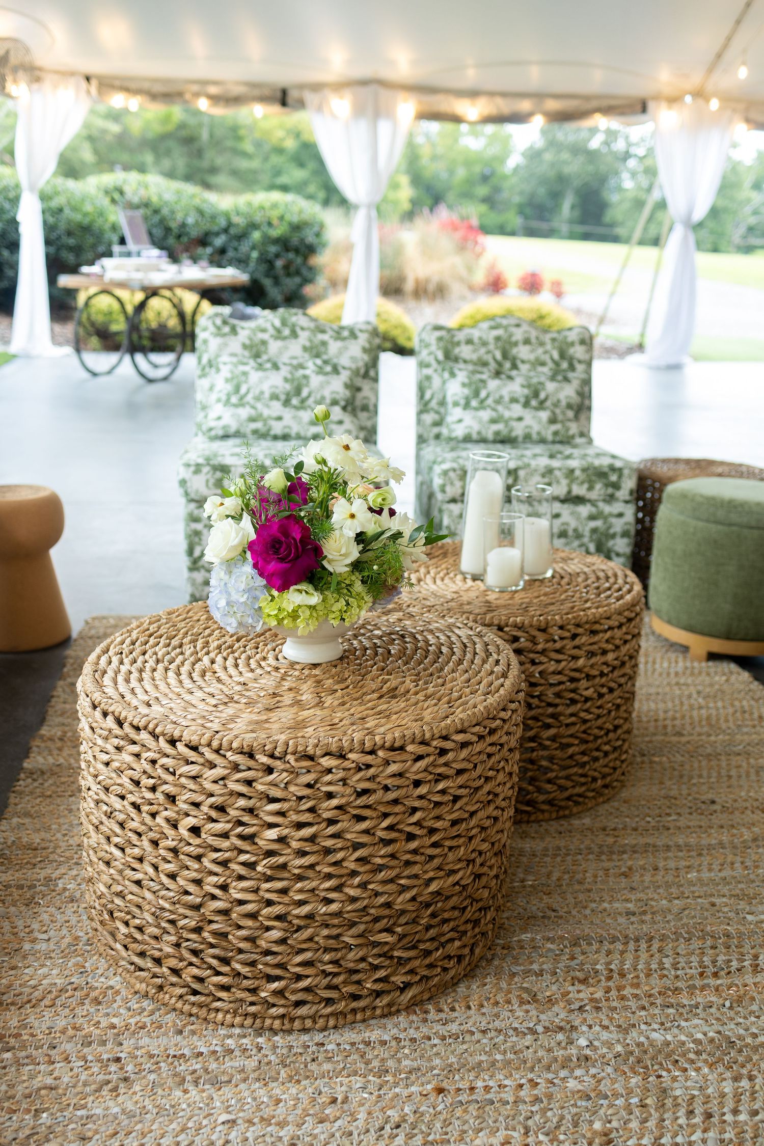 Woven seagrass pouf ottomans with delicate floral centerpieces arranged on rustic table at outdoor wedding reception.