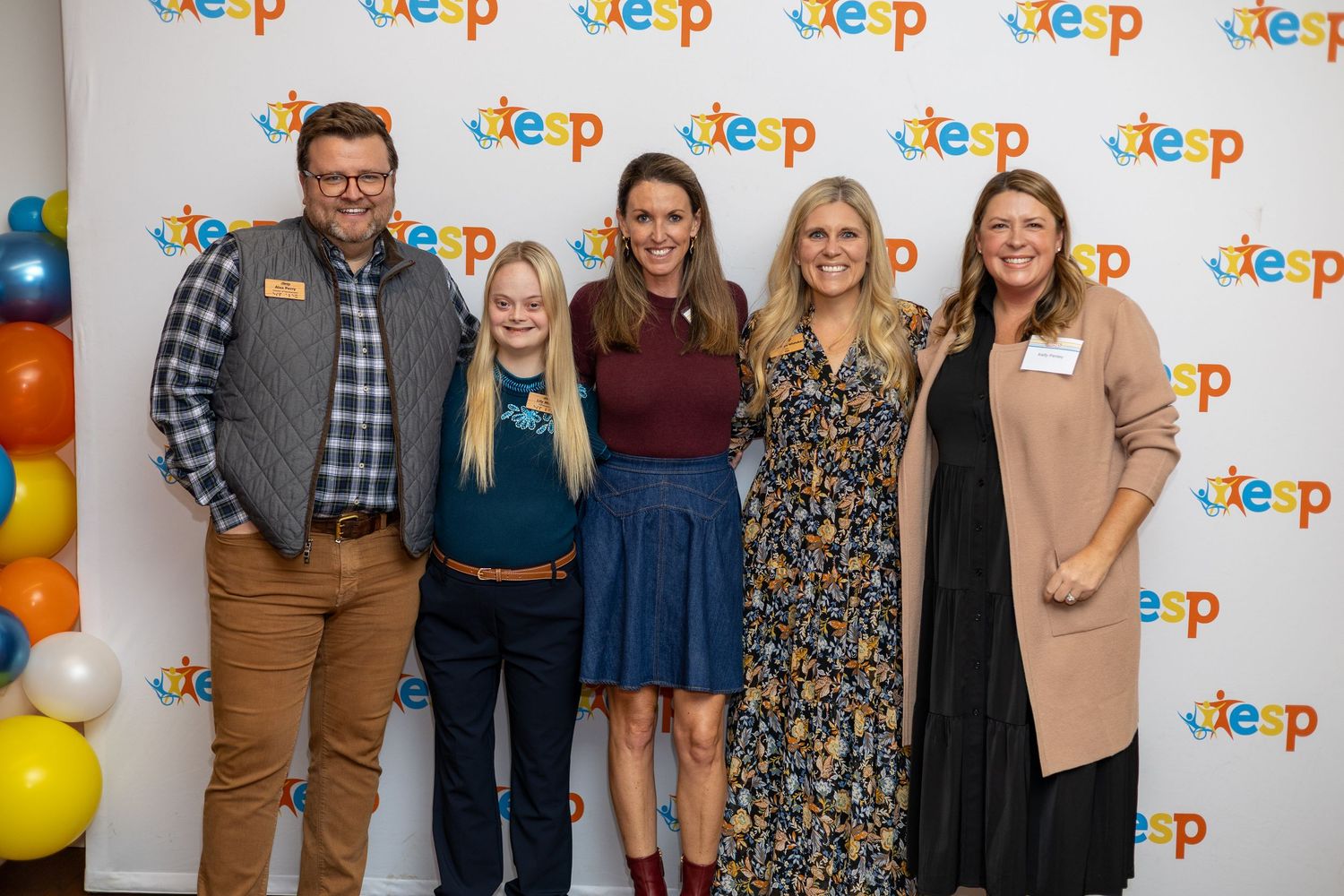 Five people smile together at a colorful TESP event with balloon decorations in the background.
