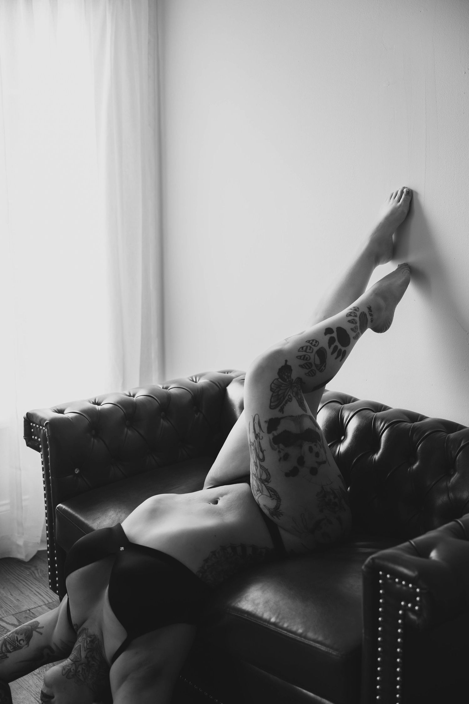 Black and white artistic portrait series showing reclining poses on a leather couch with dramatic lighting.
