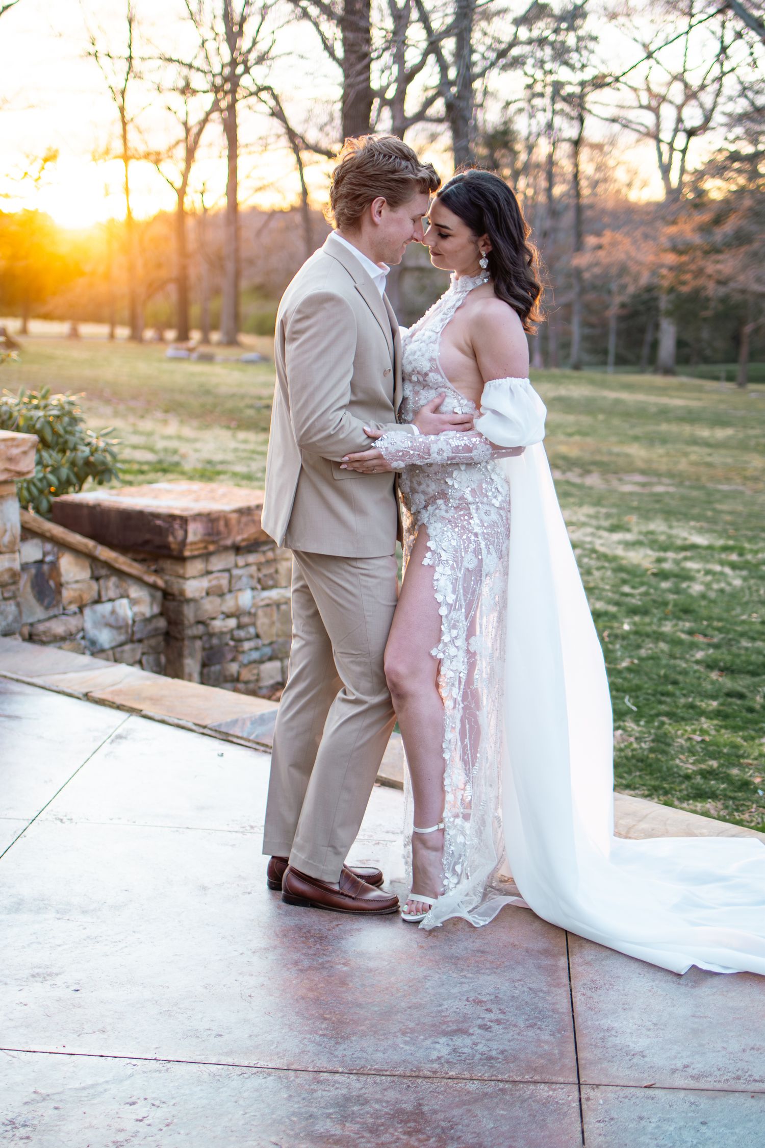 Couple shares romantic sunset moment on stone patio during outdoor spring wedding celebration.