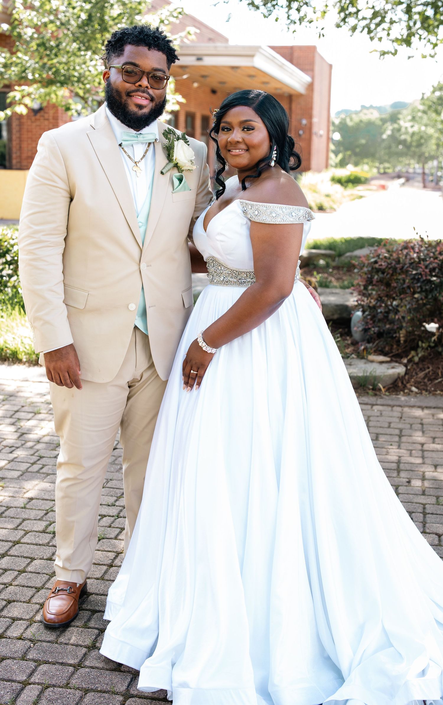 Elegant wedding portrait of a couple in cream and white attire standing on a paved outdoor walkway.