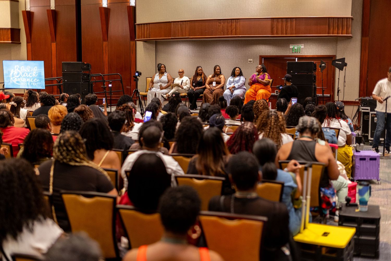 Diverse audience attends a panel discussion with speakers seated at front of a conference room.
