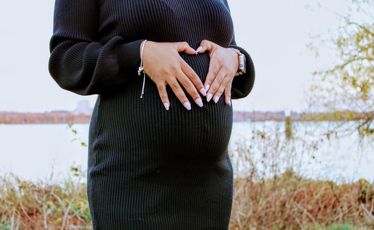Woman in black ribbed sweater poses in fall outdoor scenery showing detail of the knitwear texture and fit.