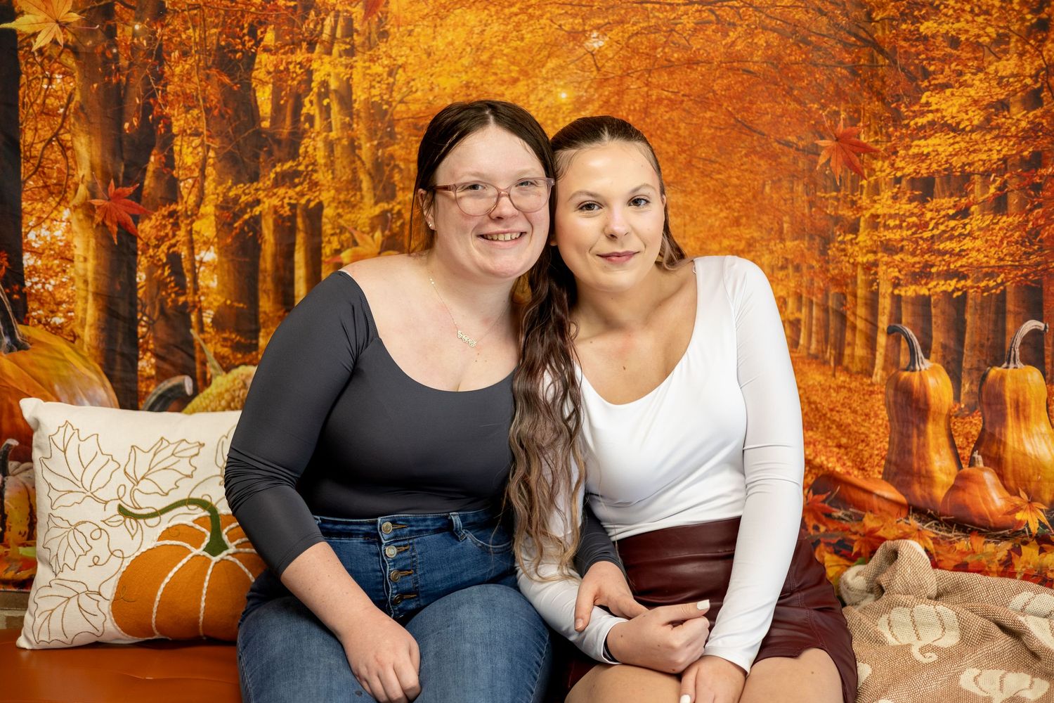 Two people embrace while posing for a fall photo shoot surrounded by vibrant orange autumn foliage in the forest.